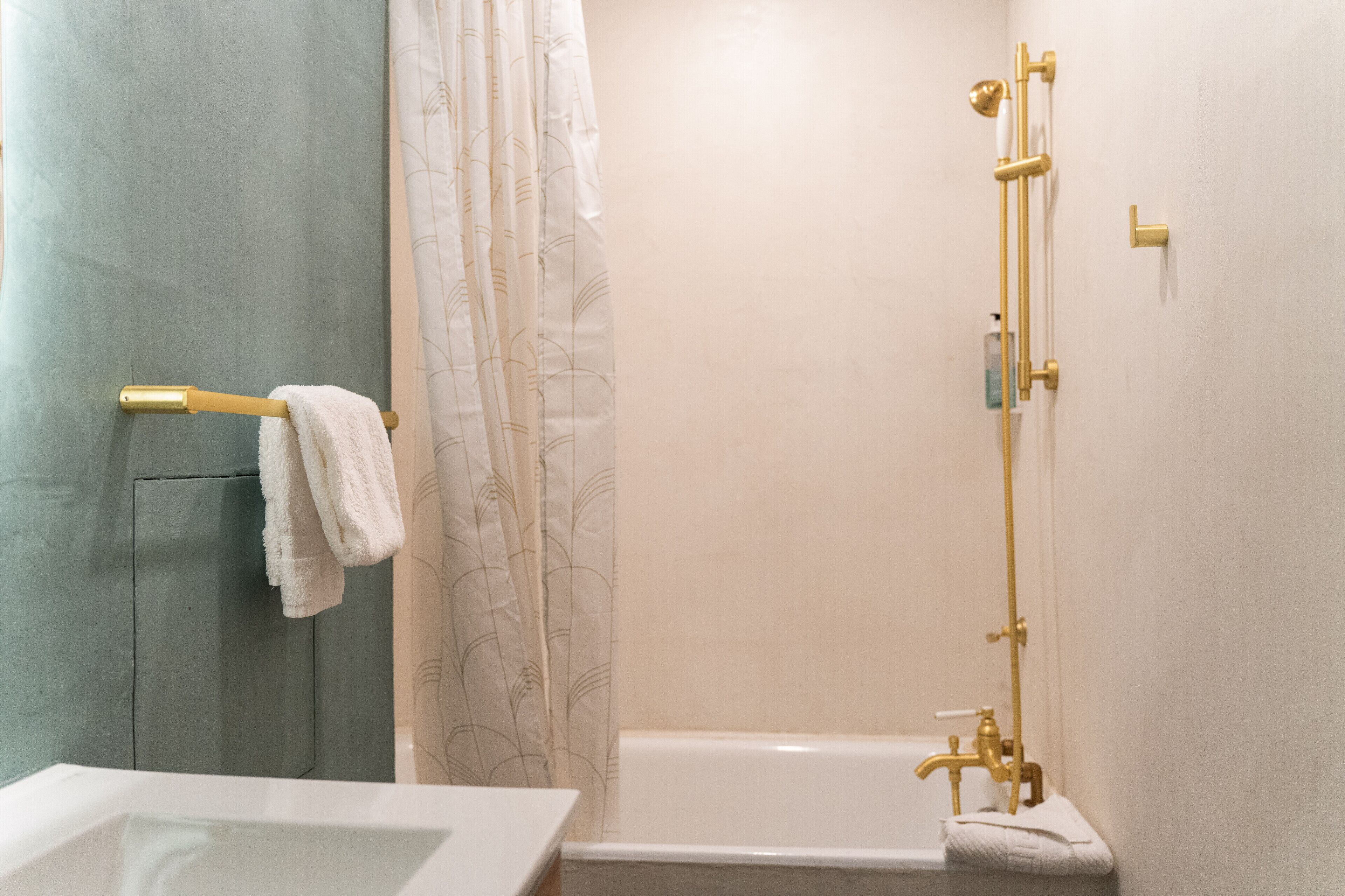 Une salle de bain avec une baignoire, une douche dotée de robinetterie dorée et un porte-serviettes avec une serviette blanche.