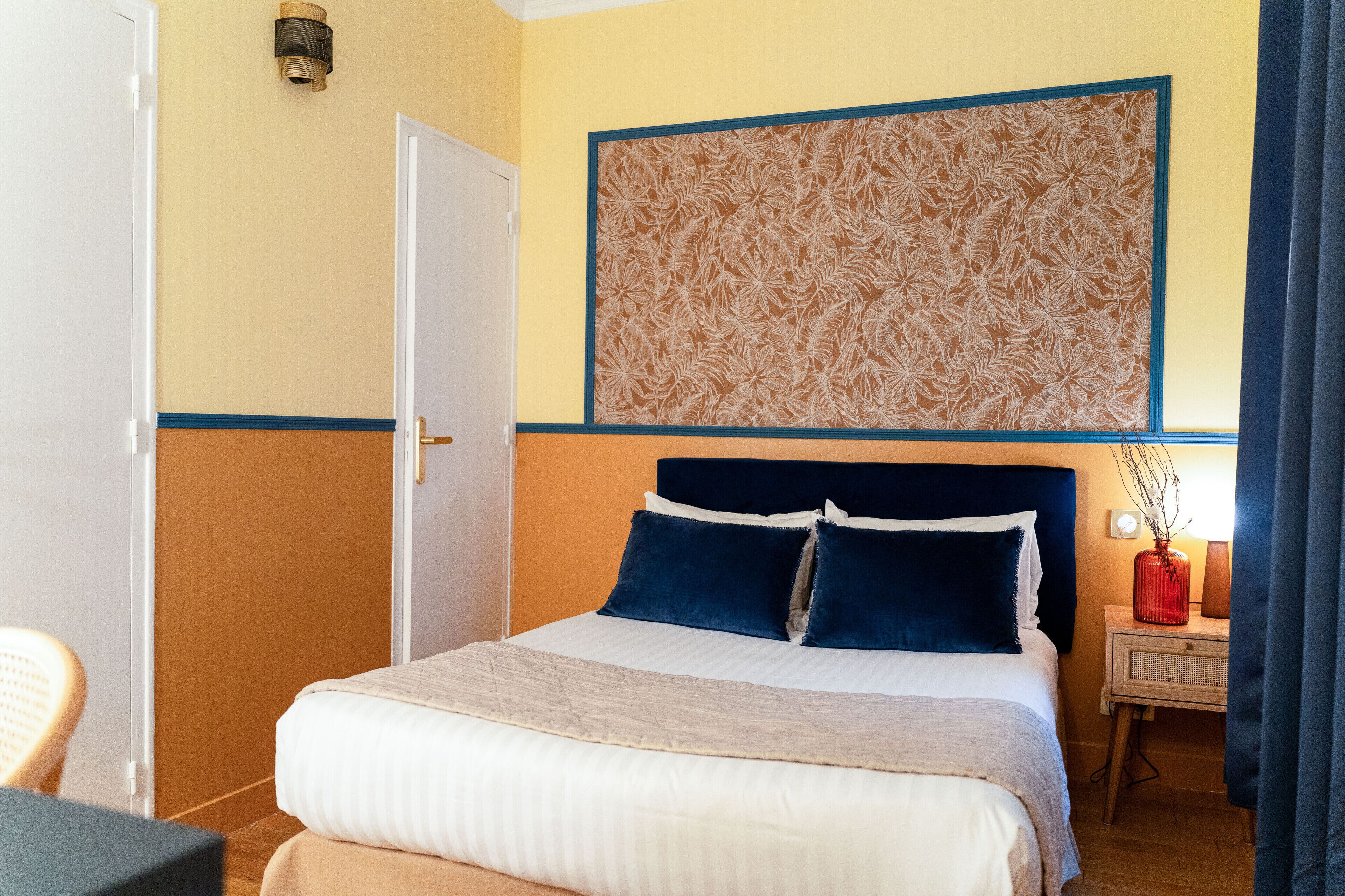 Une chambre d’hôtel comprenant un lit, une table de chevet, un panneau décoratif au mur et une porte.