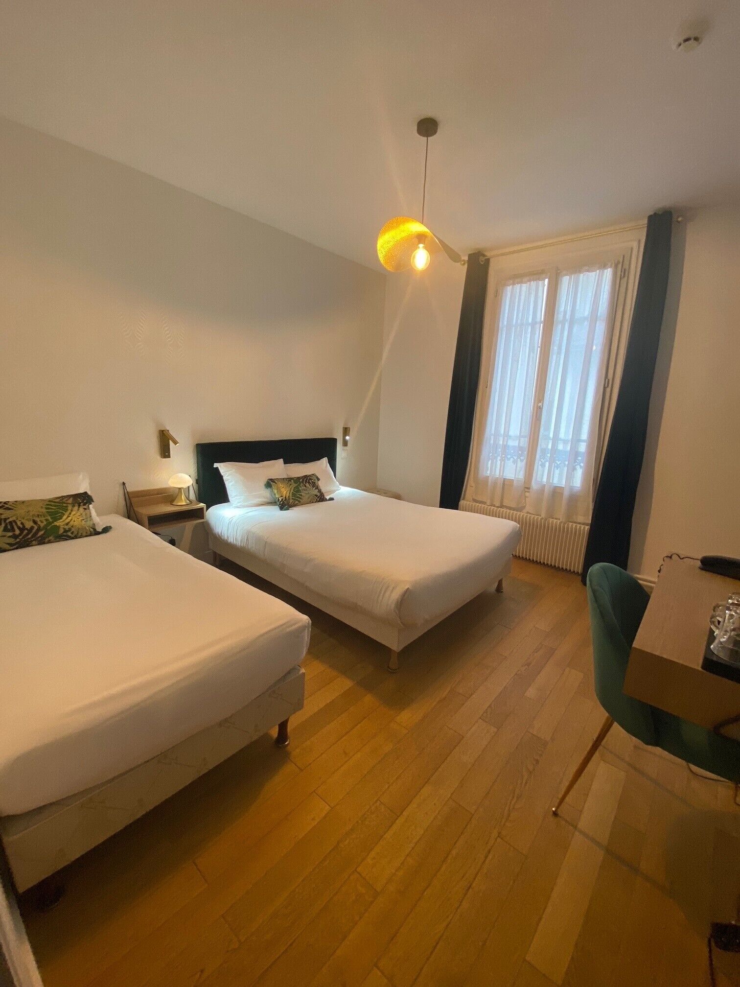 A hotel room with two beds, a desk, a chair, and a window with curtains.