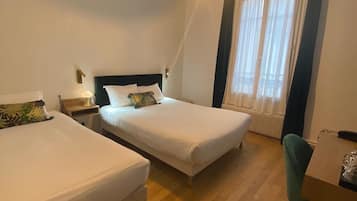 A hotel room with two beds, a desk, a chair, and a window with curtains.