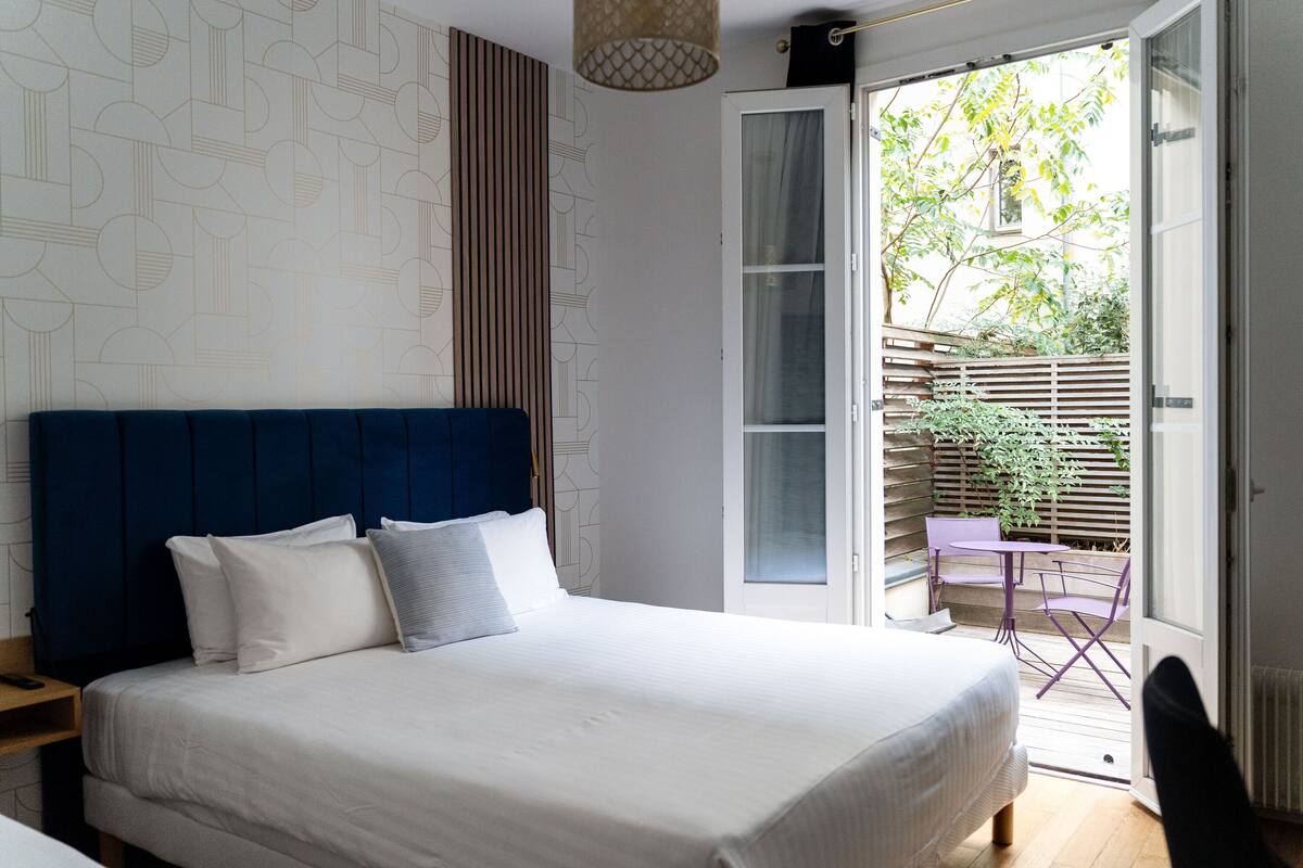 A bedroom with a large bed, a wooden headboard, and a view of an outdoor patio with a table and chairs.