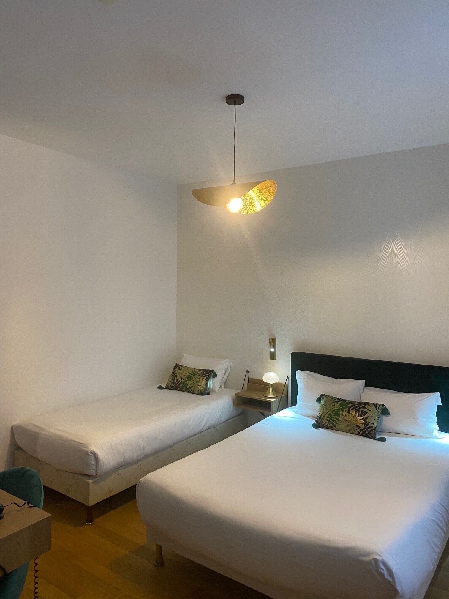 A hotel room with two single beds, a small table, and a lamp.