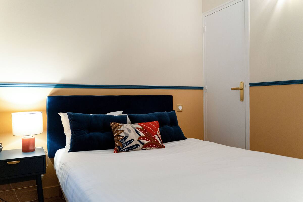 A hotel room with a bed, a nightstand, a lamp, and a door.
