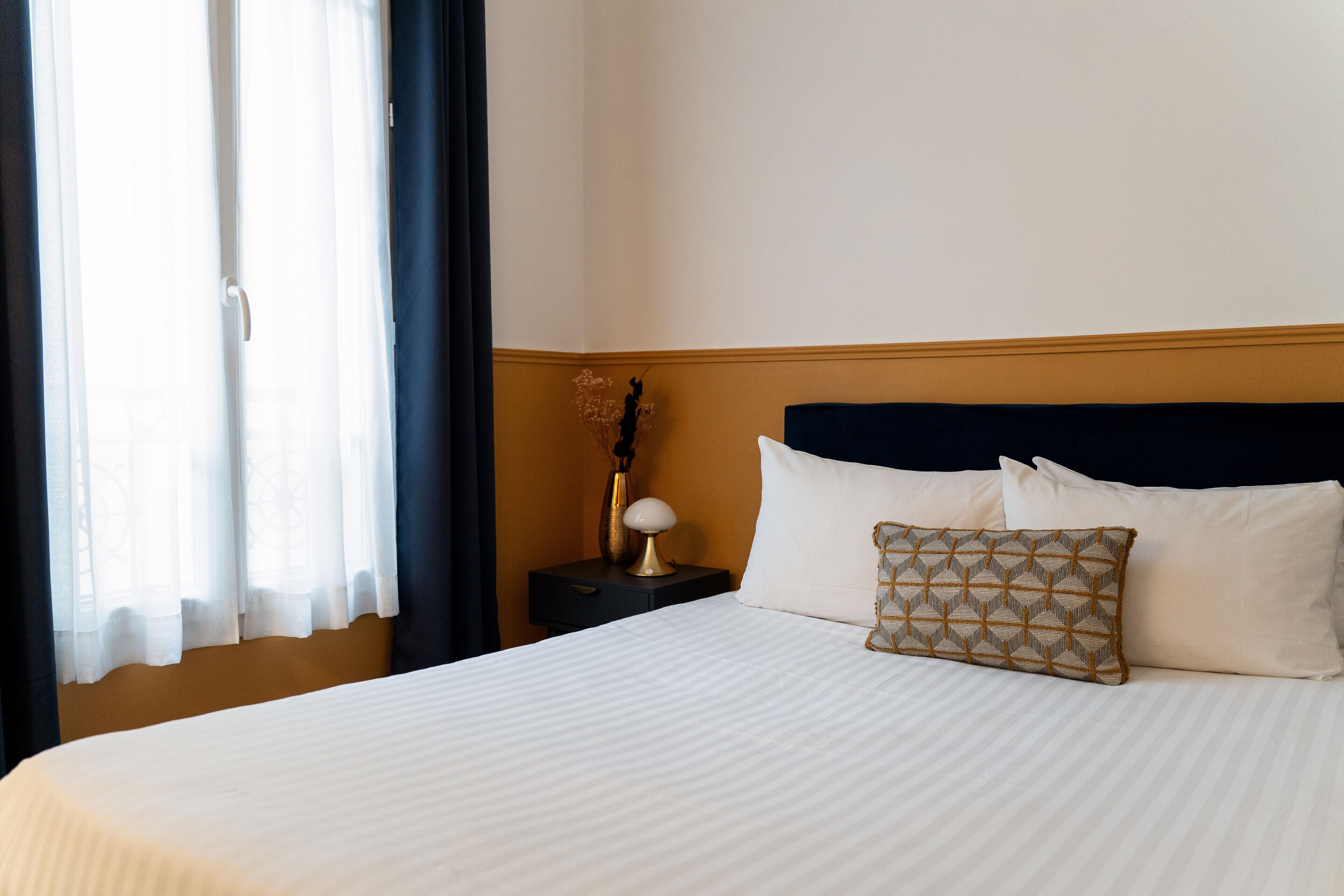 Una cama bien hecha con sábanas blancas, cabecero oscuro y almohada decorativa.