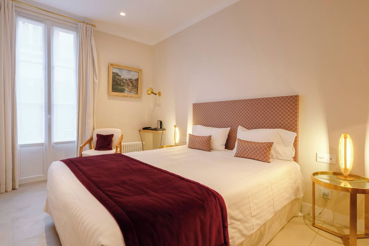 A neatly arranged hotel room with a large bed, a chair, a bedside table, and a lamp.