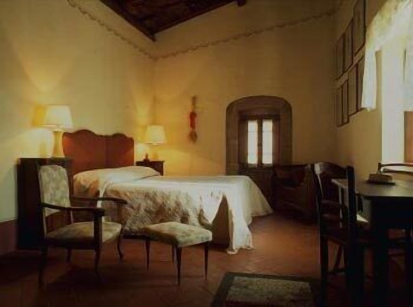 Una habitación tradicional con una cama, dos sillas, una mesita y una ventana.