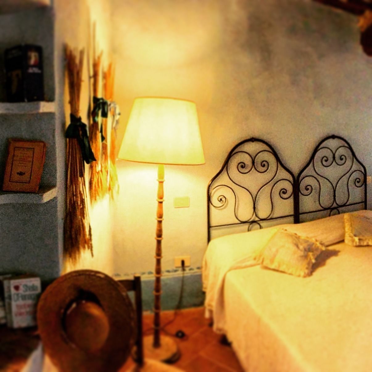 A bedroom with a bed, a lamp, a hat, and a wall-mounted shelf with items.