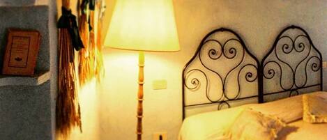 A bedroom with a bed, a lamp, a hat, and a wall-mounted shelf with items.