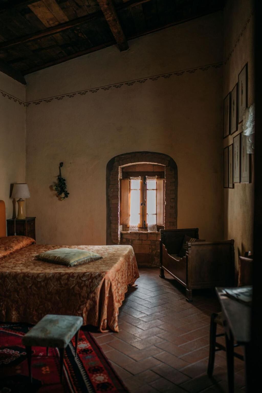 Un dormitorio con una cama grande, una silla de madera, una mesita y un ventanal con vistas al exterior.