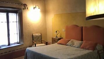 Un dormitorio con una cama, una silla, una mesita de noche, una lámpara, un ventanal y techo de madera.