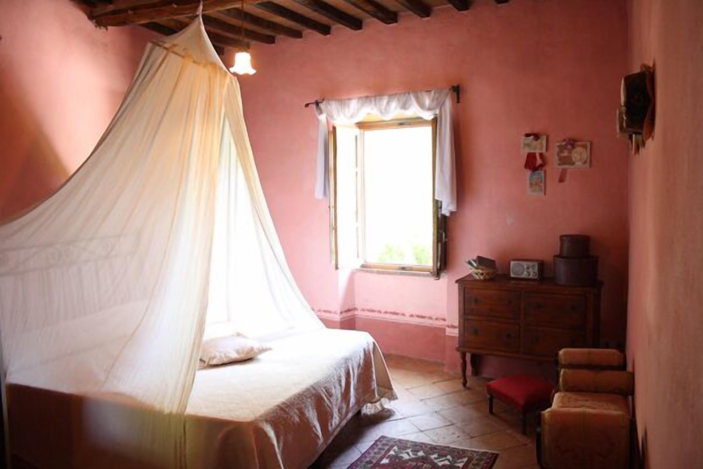 A bedroom with a canopy bed, a dresser, a window with curtains, and a small table with a radio.