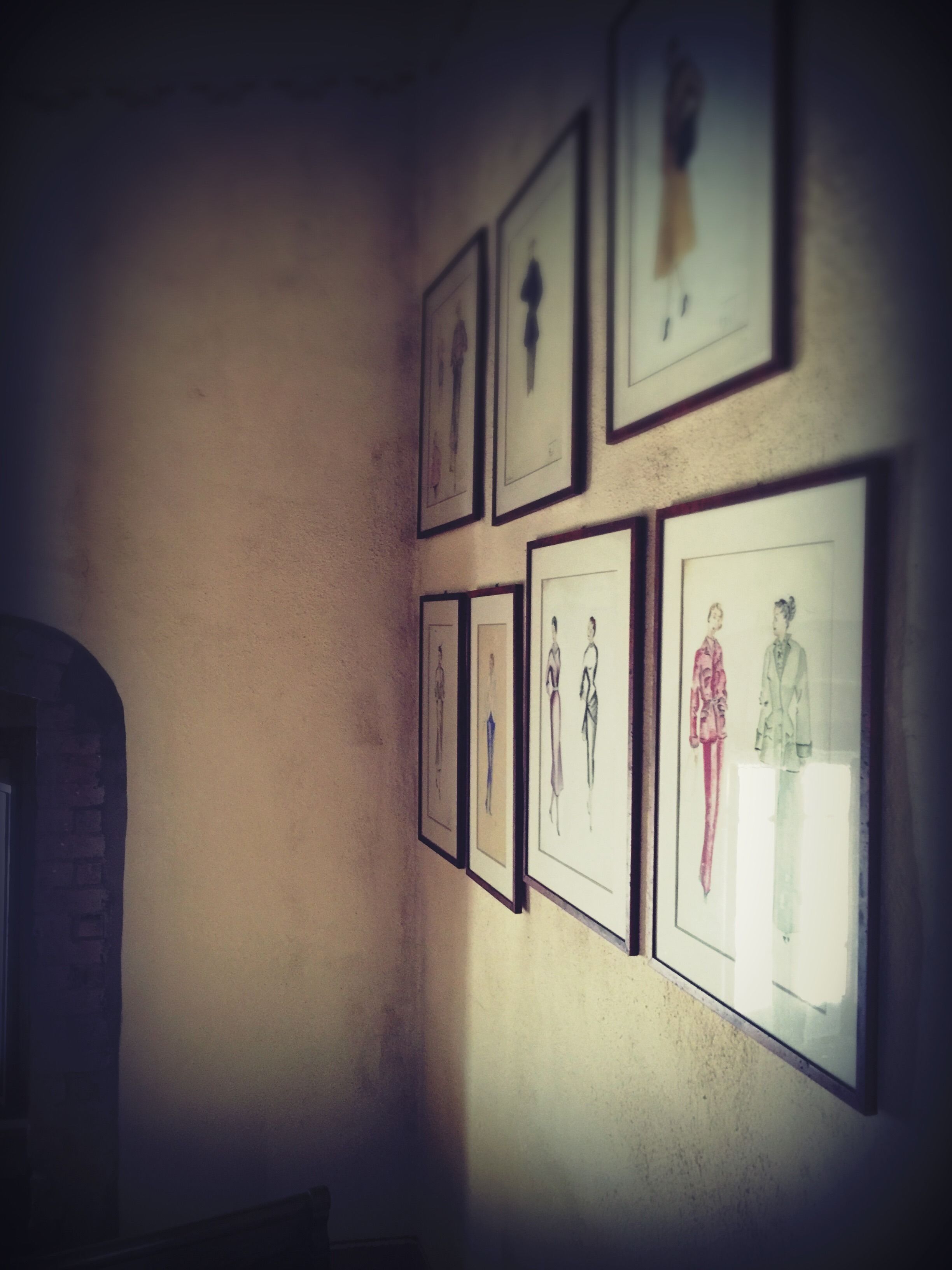 A wall with multiple framed sketches of fashion designs.