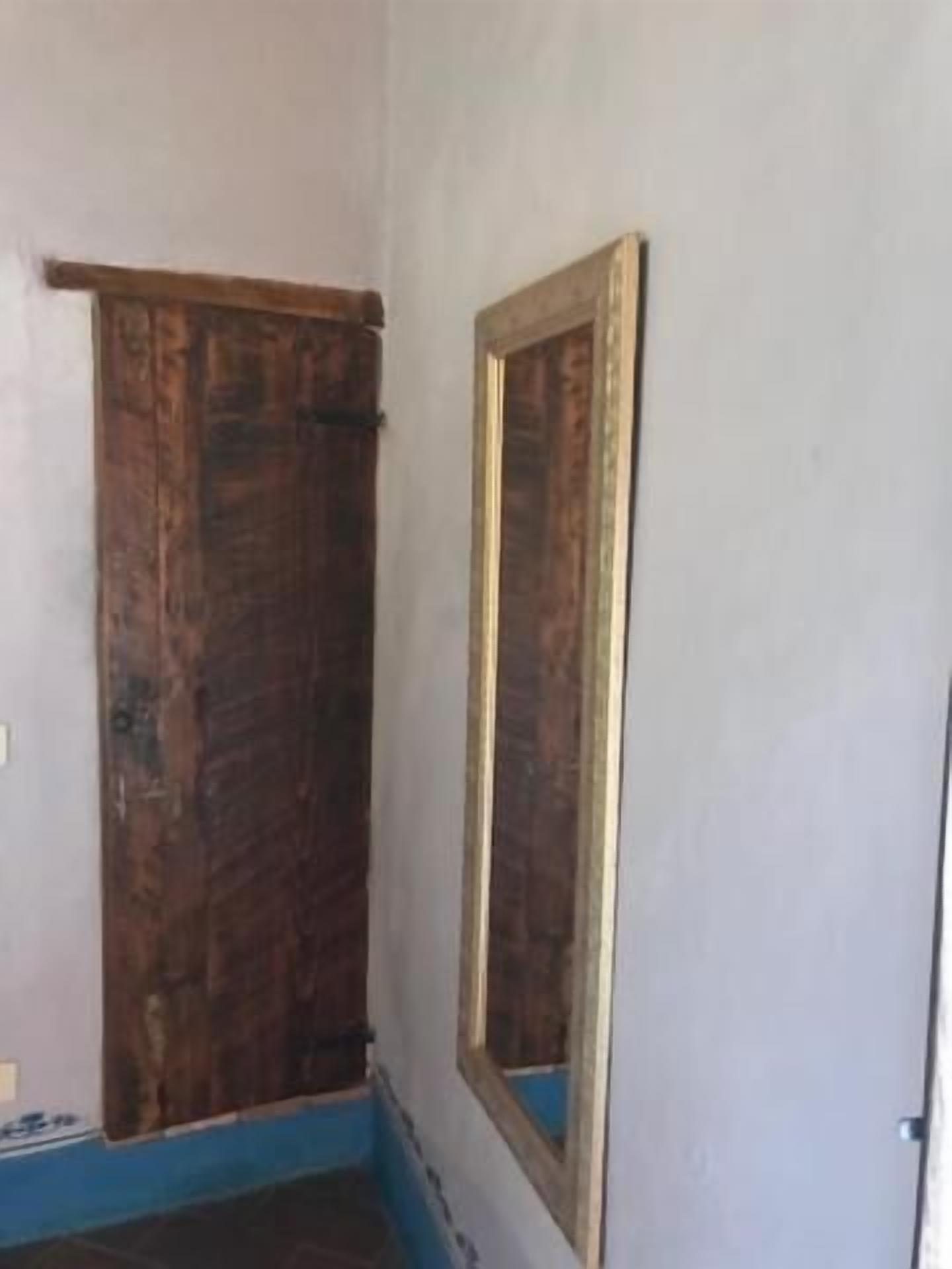 Une pièce avec une porte en bois, un miroir et le bas d’un mur peint en bleu.