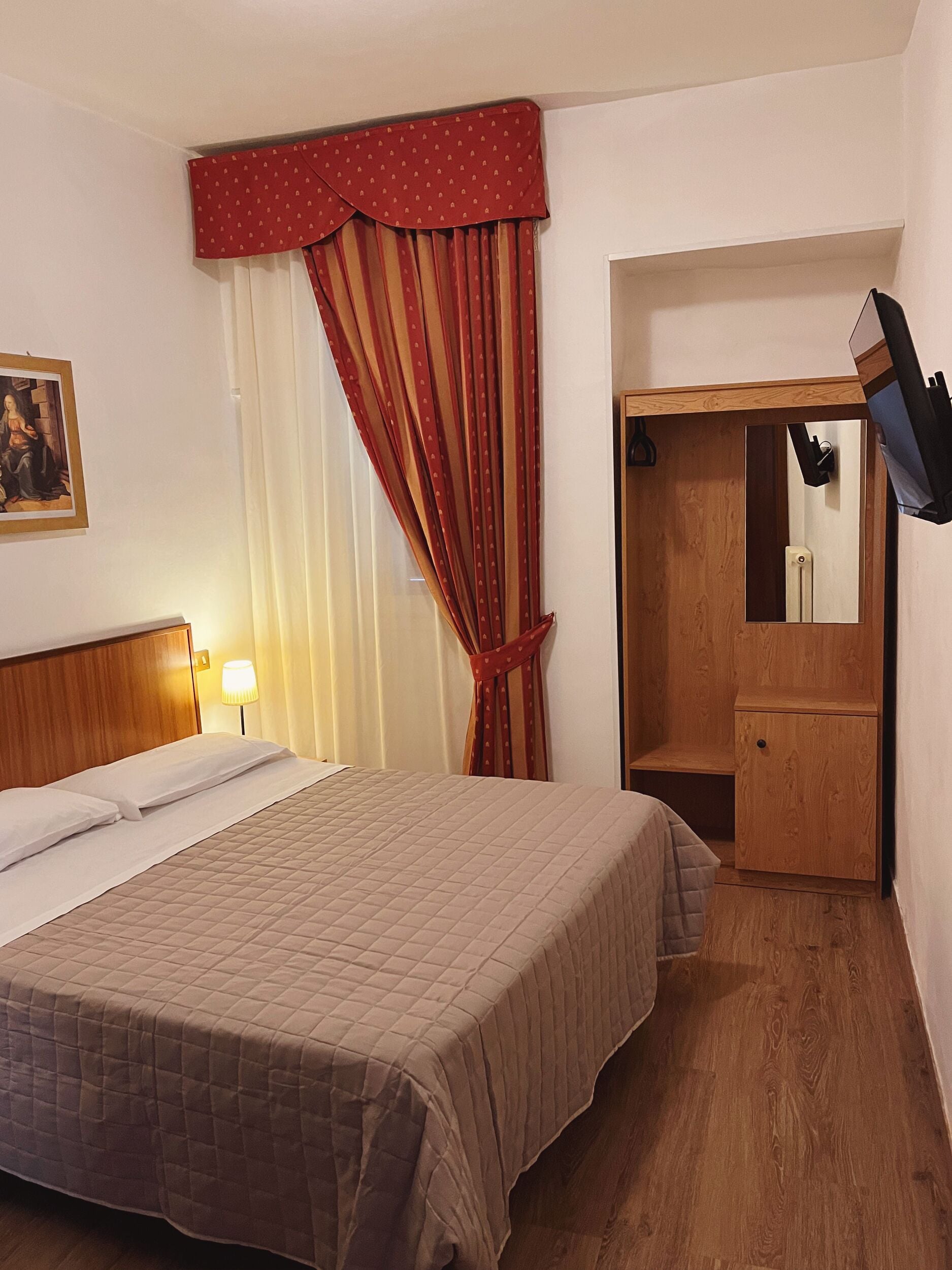 Habitación de hotel con cama, armario de madera, espejo y un cuadro en la pared.