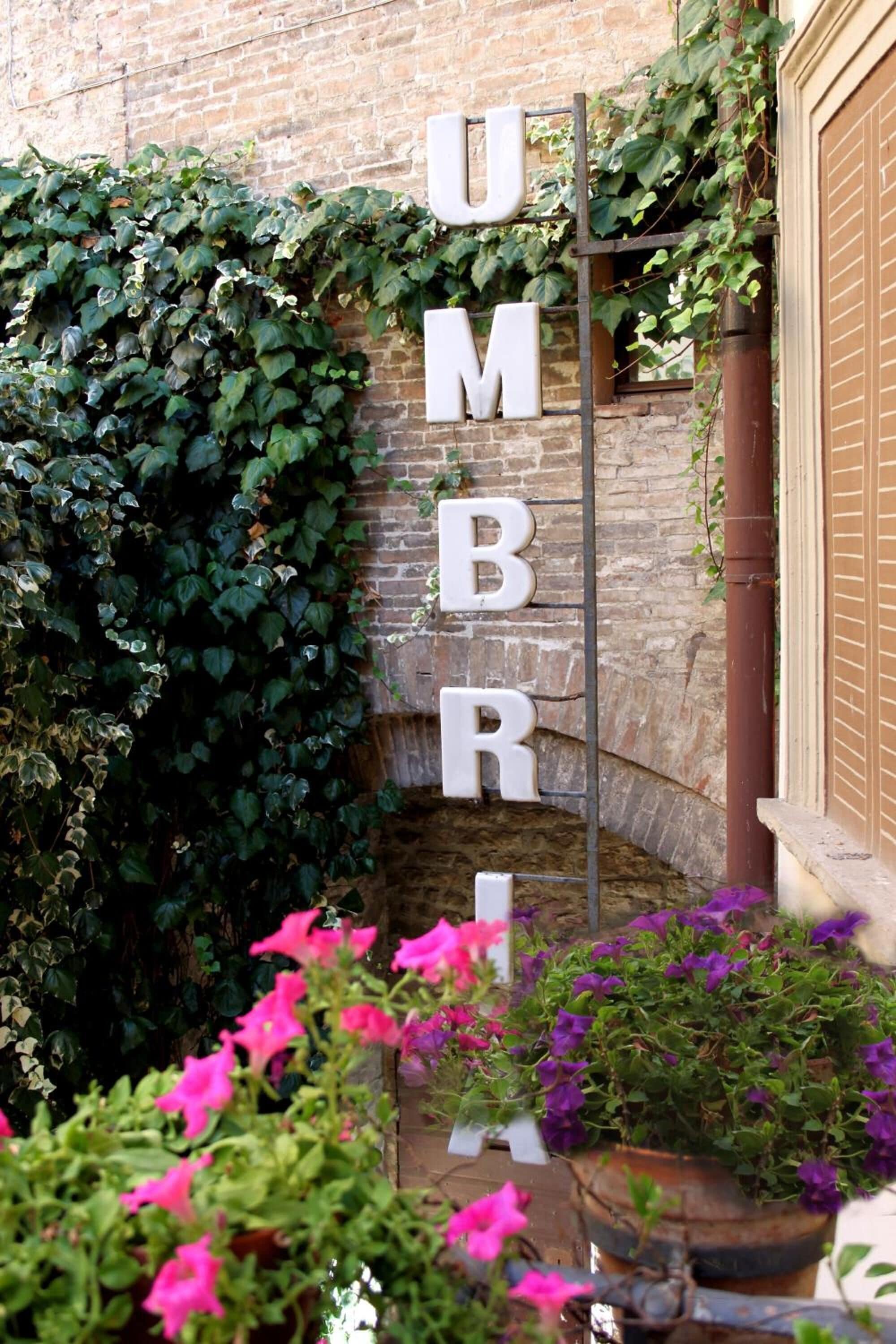 Un jardín con un letrero de metal que dice 'UMBRI' y diferentes macetas con plantas.