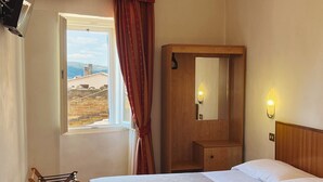 Habitación de hotel con cama, mesita de noche de madera, espejo, ventana con cortinas y vistas al exterior.