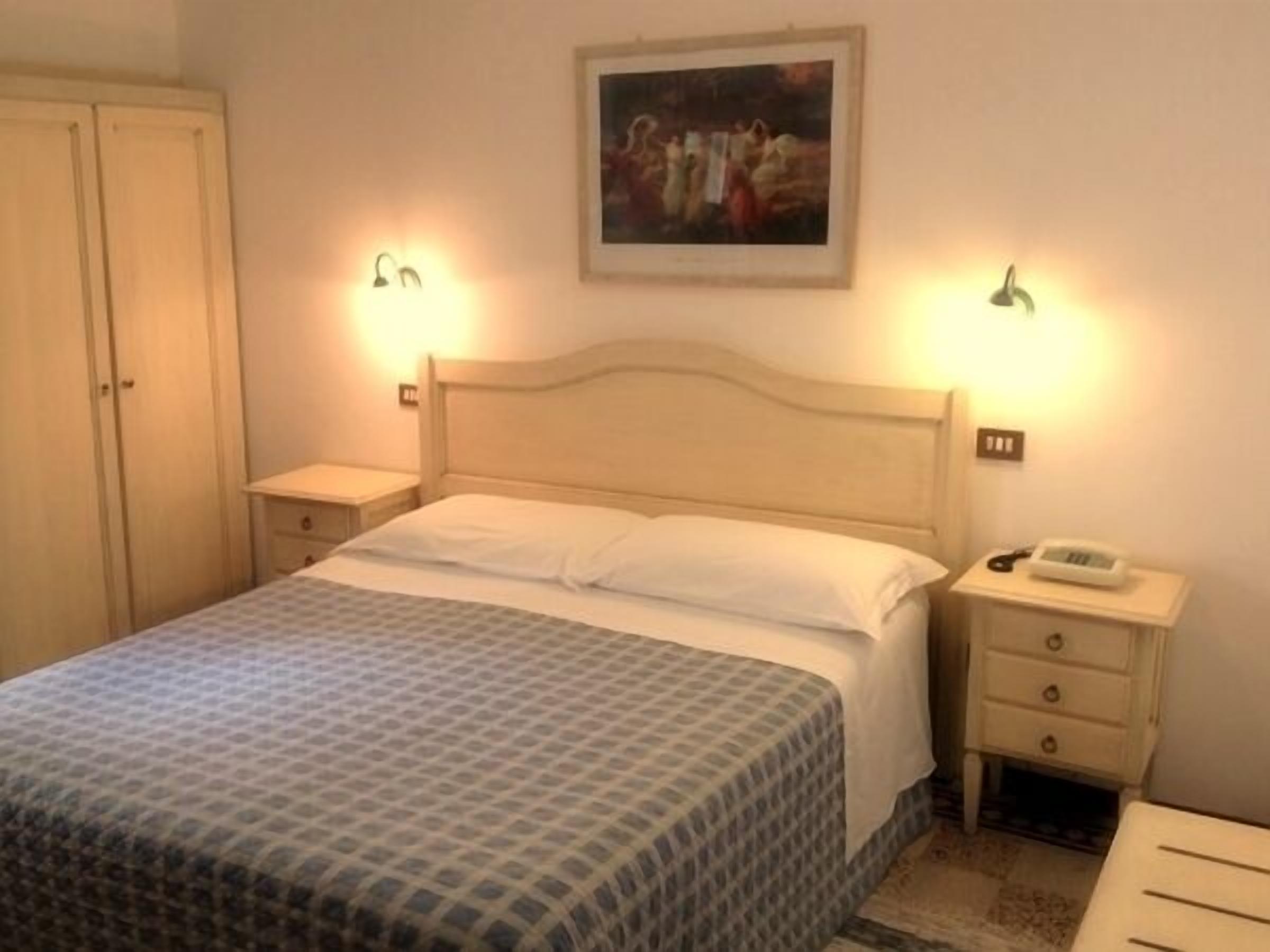 A bedroom with a bed, bedside tables, a wardrobe, and a painting on the wall.