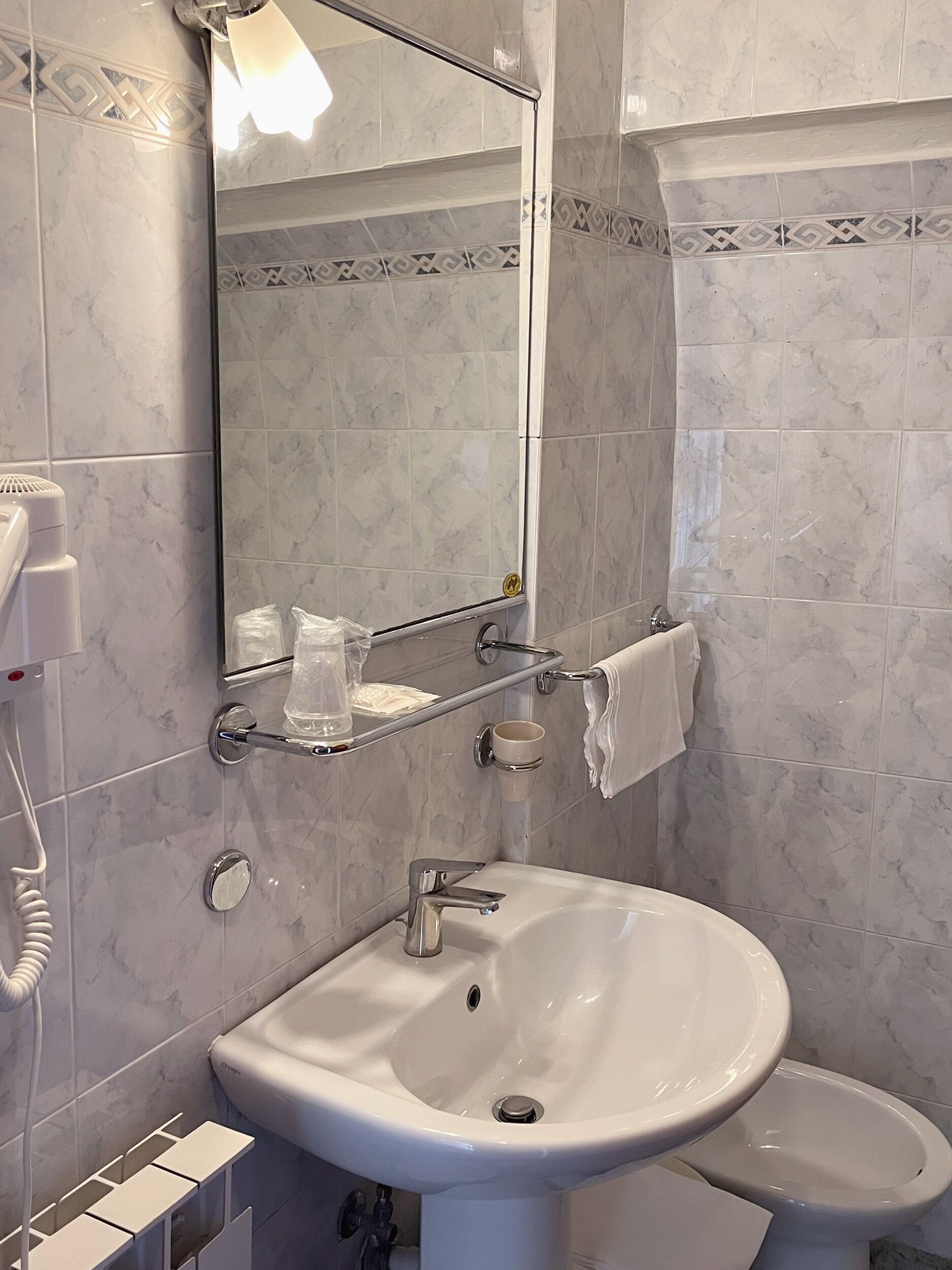 A bathroom with a white sink, a toilet, and a mirror. There is a towel rack with a towel hanging on it.