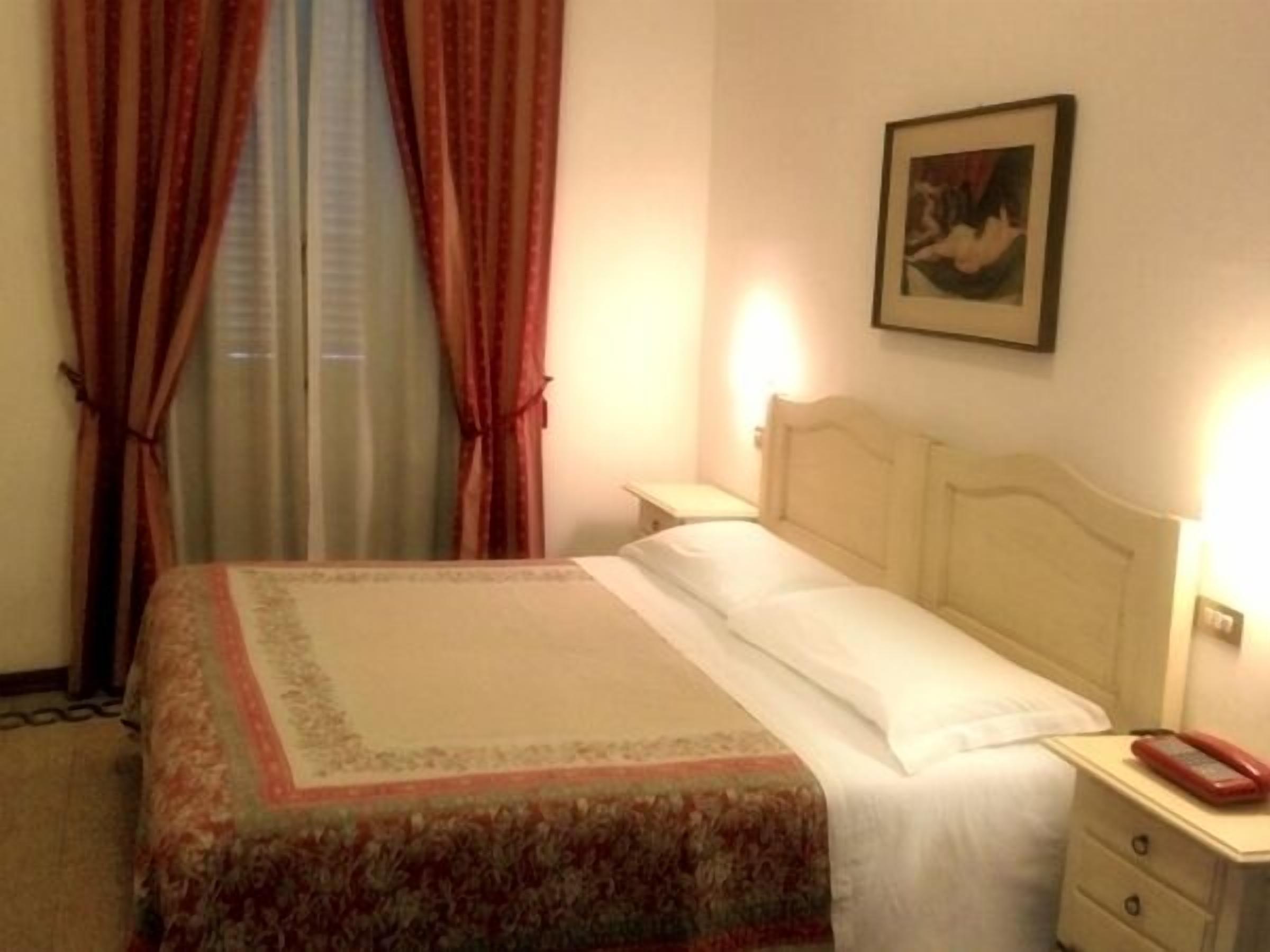 Ein Hotelzimmer mit einem Bett, einem Nachttisch, einem Telefon und einem Bild an der Wand.