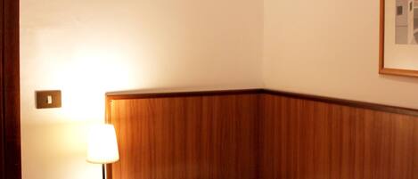 A hotel room with a wooden headboard, a bedside table with a lamp, a phone, and a bed with a patterned blanket.