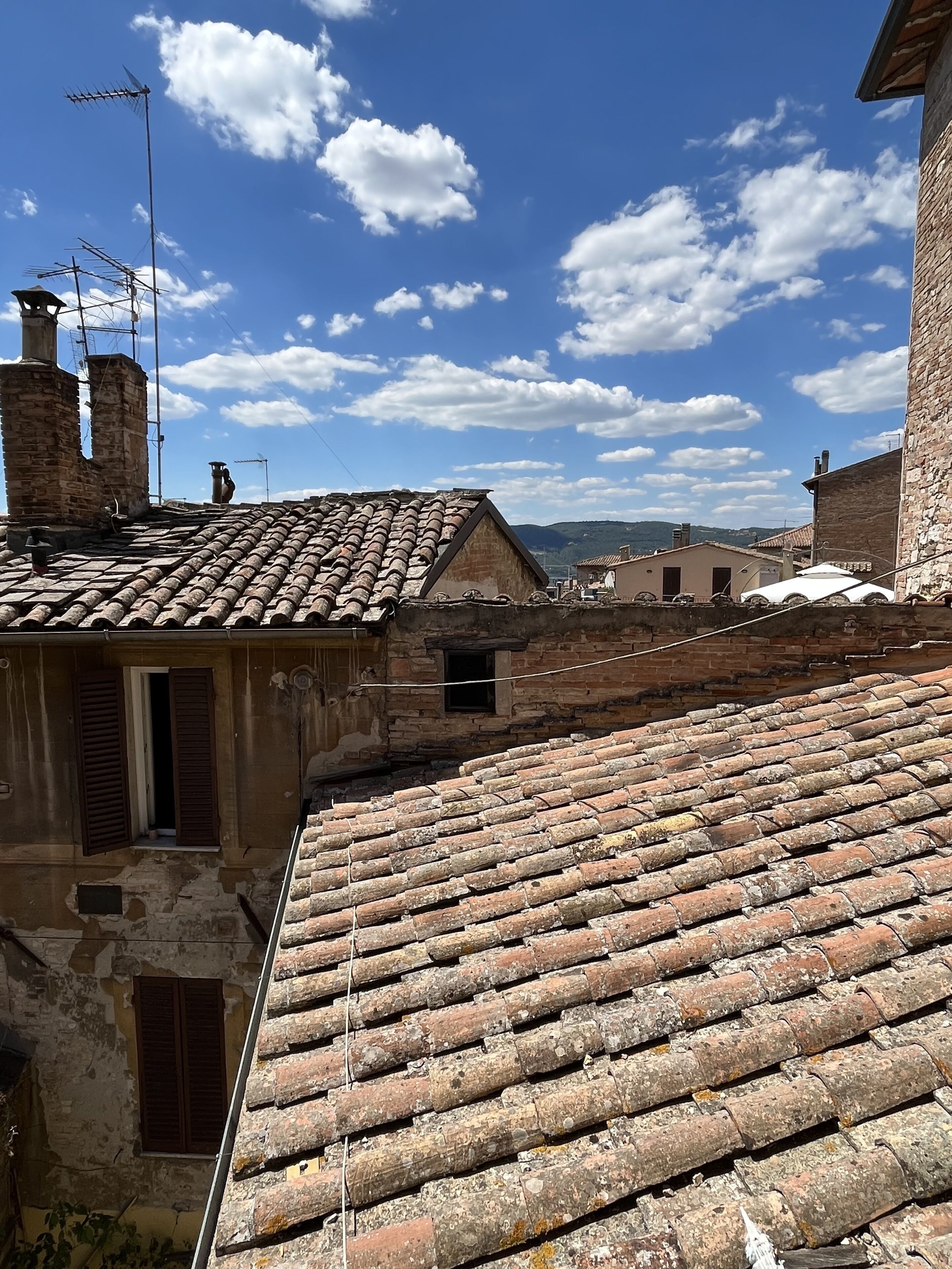 A traditional stone building with a tiled roof, a chimney, and a small window with shutters.