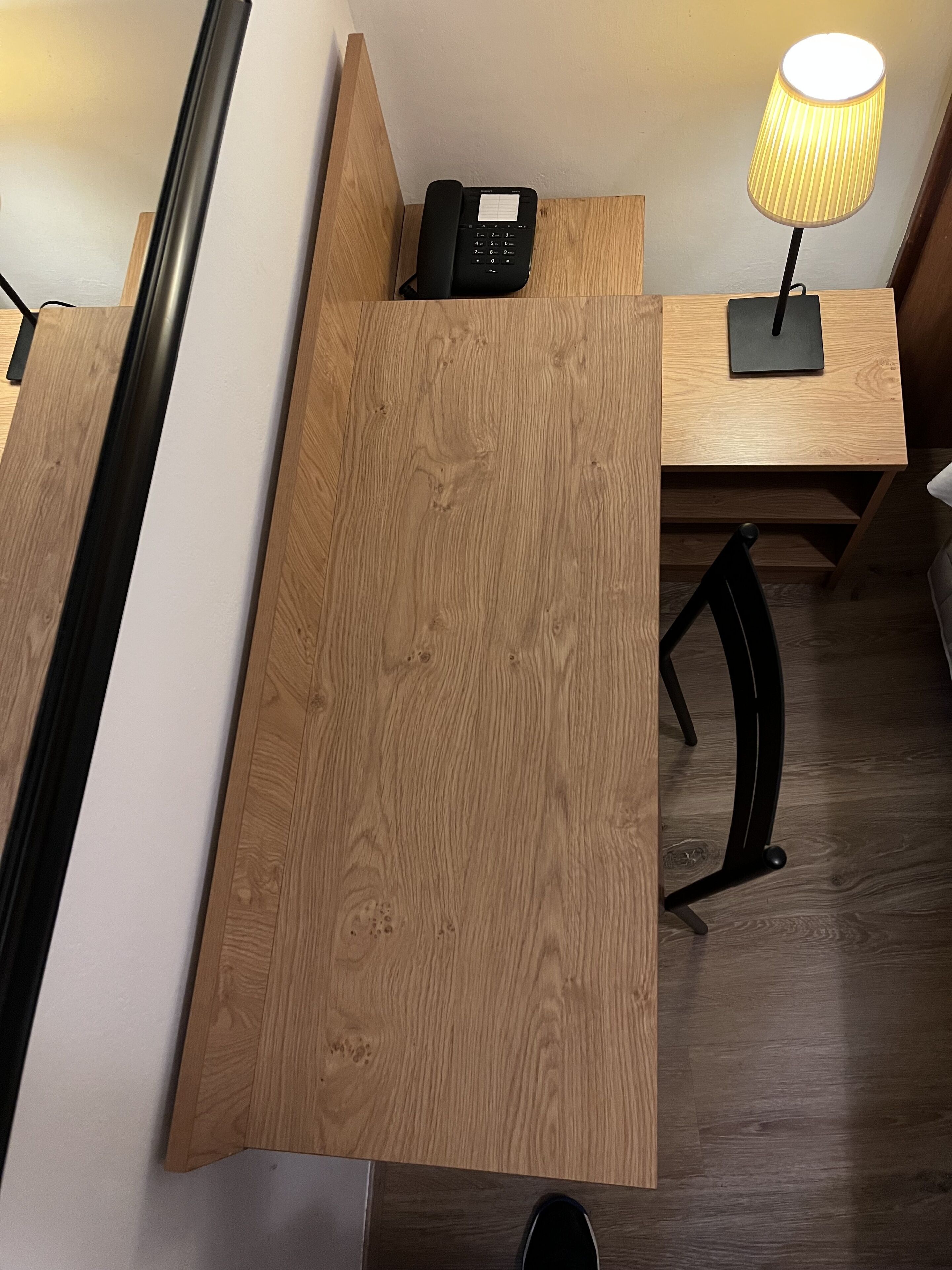 A wooden desk with a telephone and a lamp.