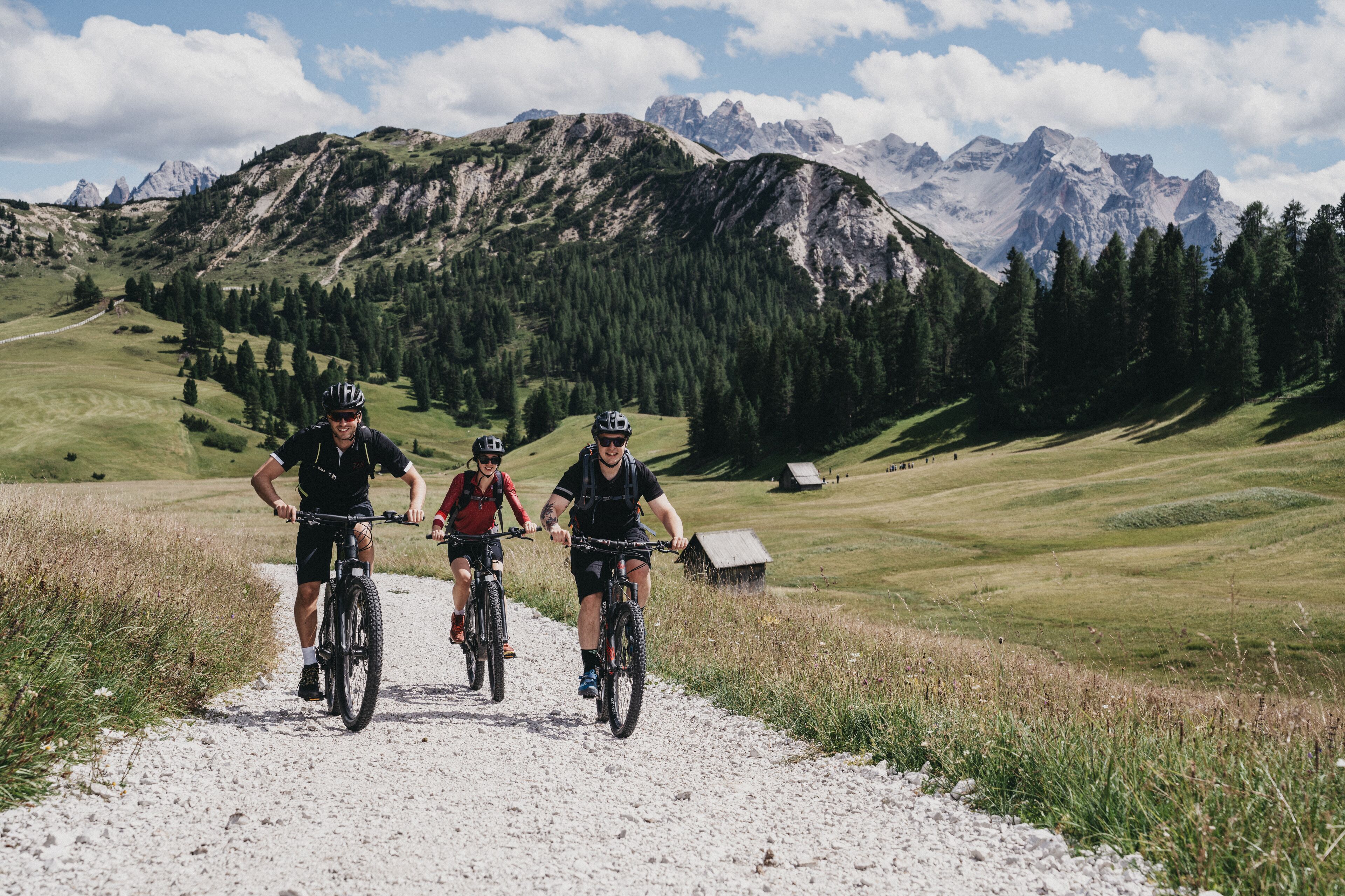 Tres ciclistas en un camino de grava con montañas al fondo.