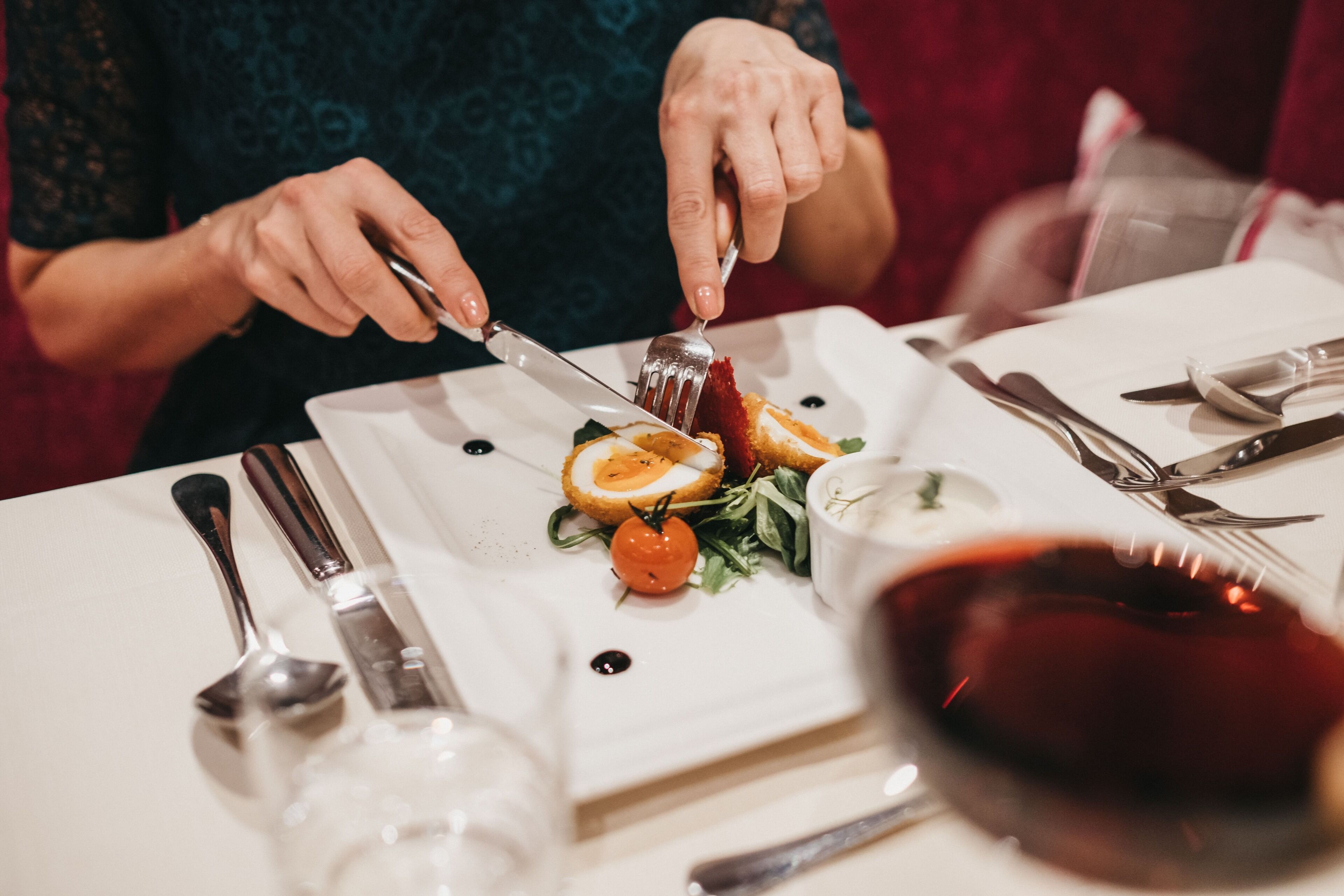 A person cutting a piece of food on a white plate with a fork and knife.