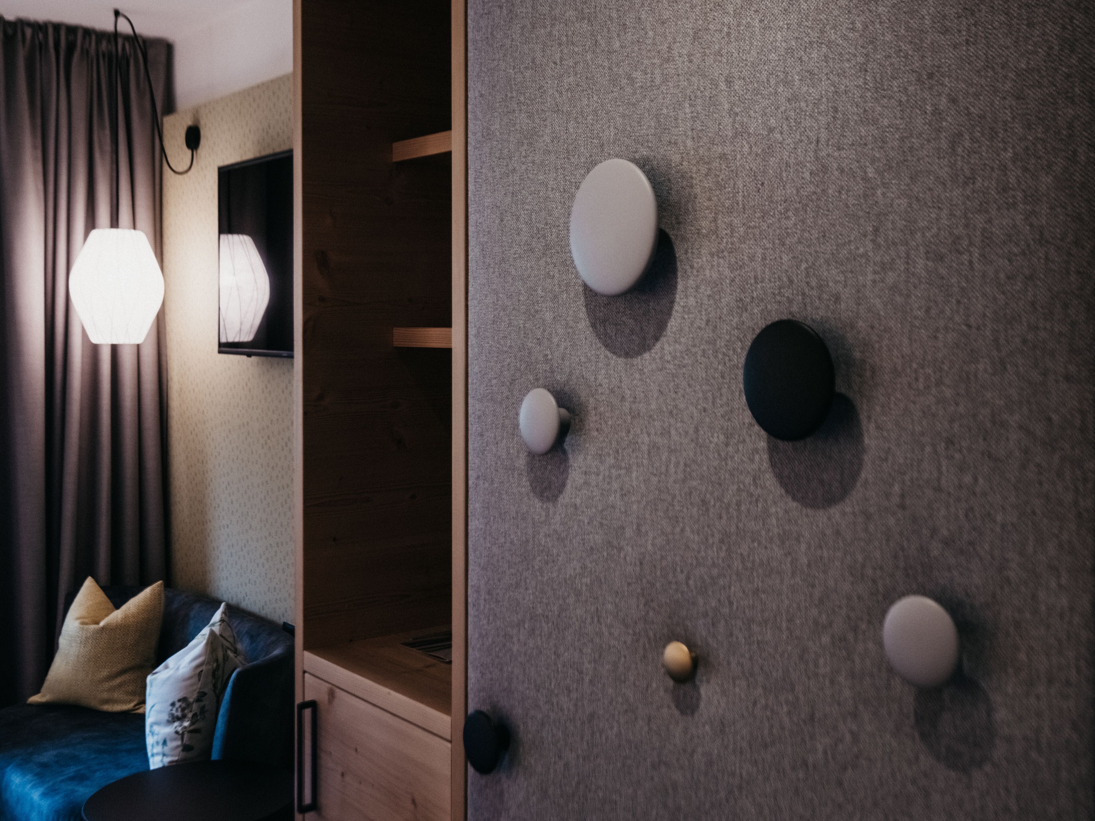 Una habitación moderna con un sofá azul oscuro, un armario de madera y una pared gris con textura y objetos redondos montados en la pared.