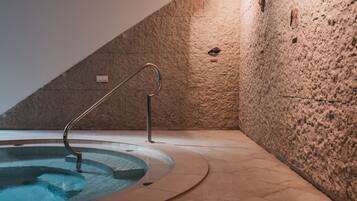Piscina interior con paredes de piedra, barandilla de metal, suelo de baldosas y techo inclinado.