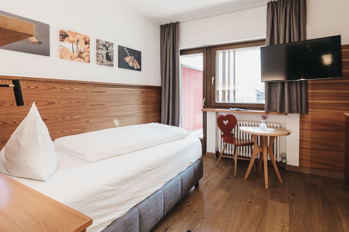 Ein Hotelzimmer mit Bett, Schreibtisch, Stuhl, Fernseher und einem Fenster mit Vorhängen.