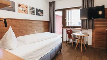 Habitación de hotel con cama, escritorio, silla, televisión y ventana con cortinas.