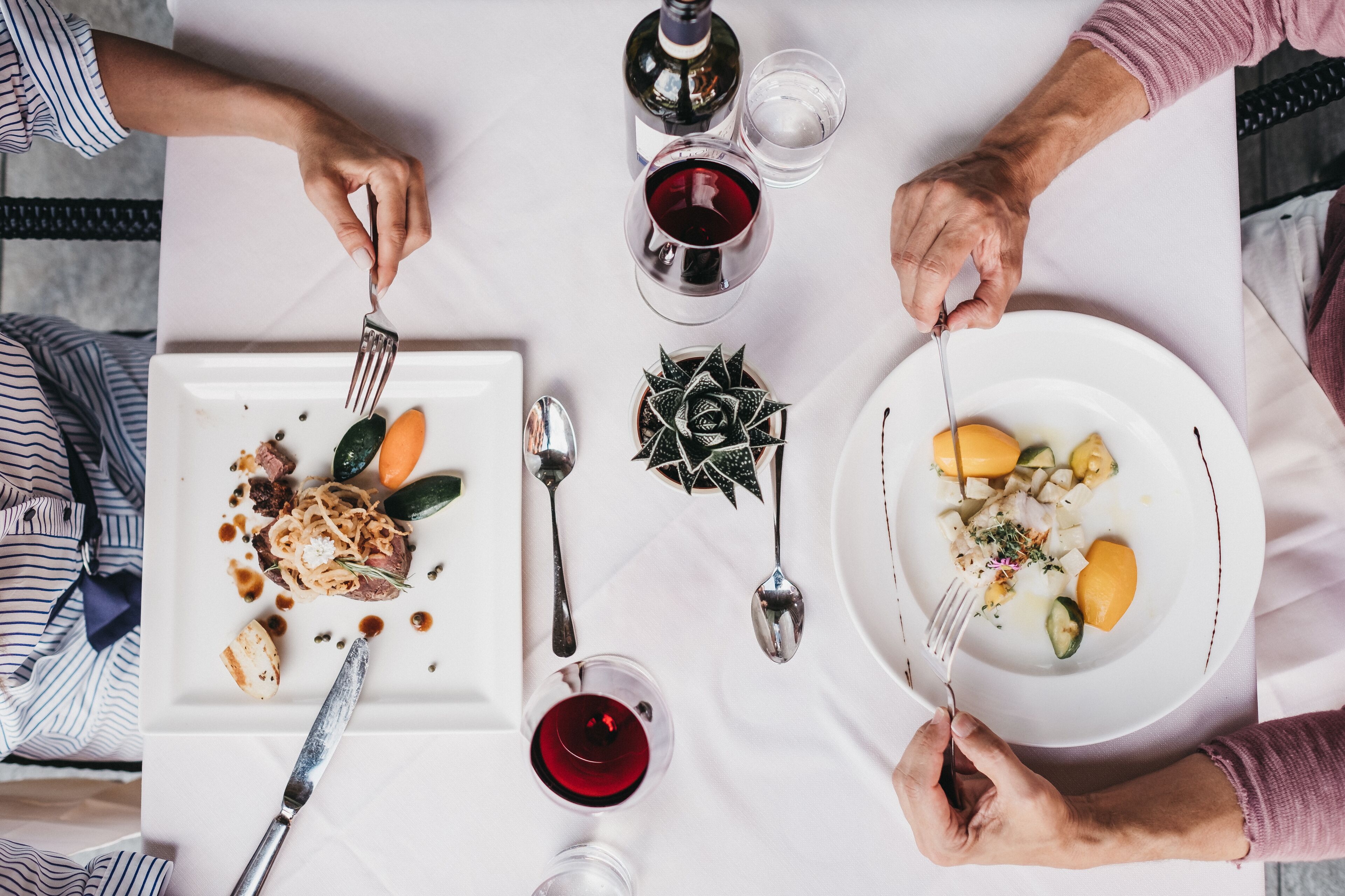 A dining table with two plates of food, a bottle of wine, and a glass of wine.
