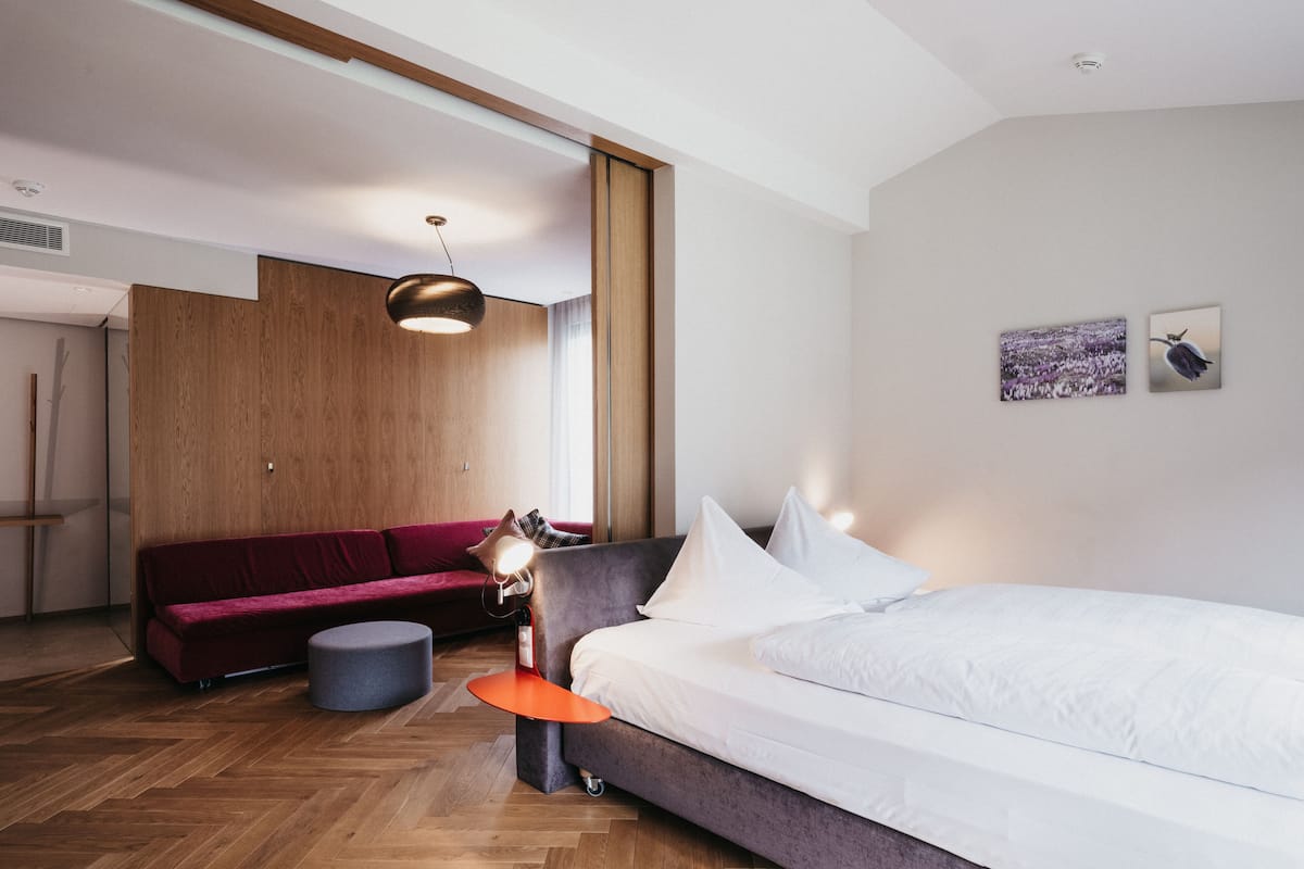 Ein modernes Hotelzimmer mit einem großen Bett, einem roten Sofa, einem kleinen runden Tisch und einer Pendelleuchte.