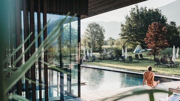 A poolside area with a view of a mountainous landscape, outdoor seating, and a glass-enclosed room. - Hotel Rudolf (Brunico)