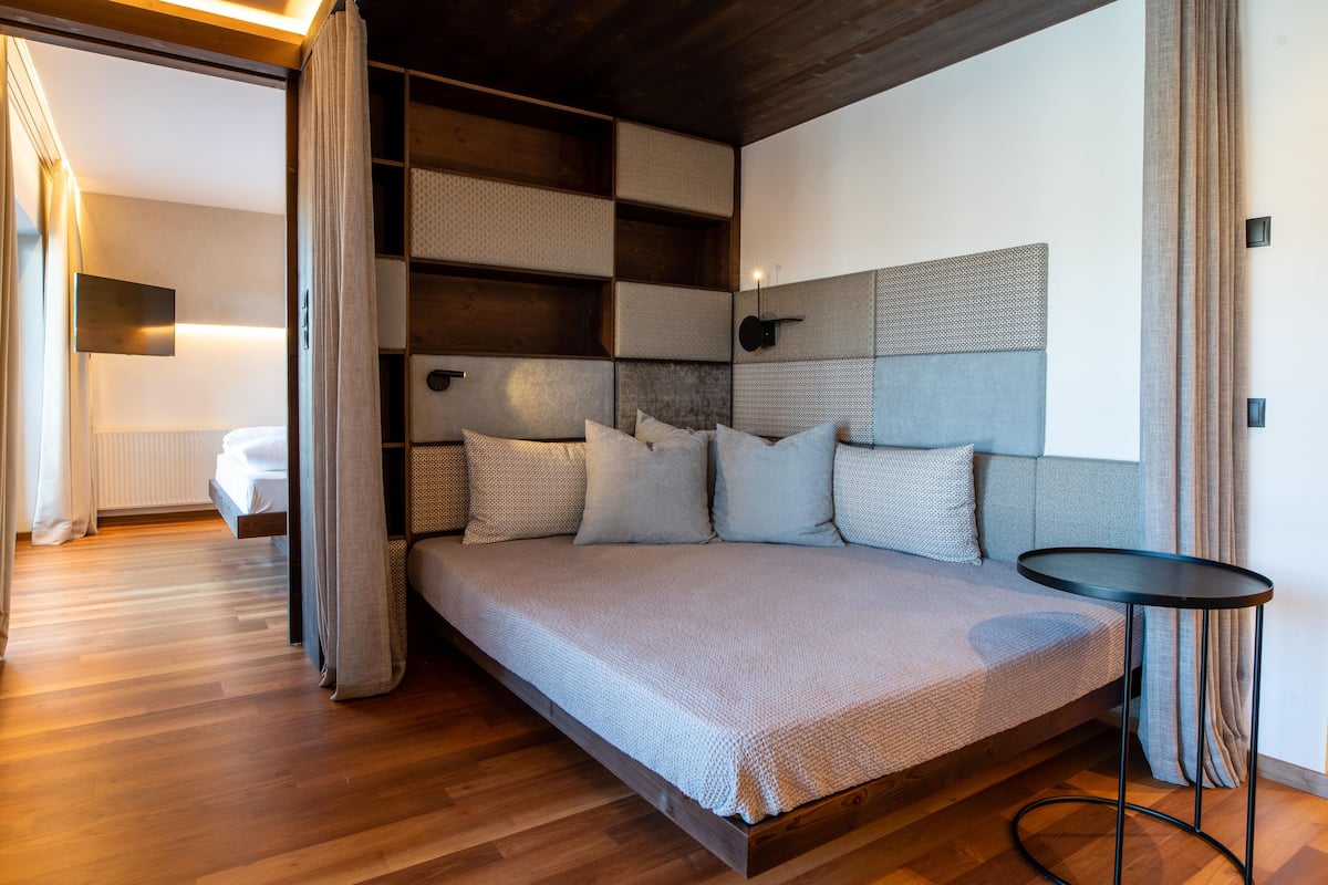 Ein modernes Schlafzimmer mit Holzboden, einem Bett mit grauem Kopfteil und einem kleinen runden Tisch.