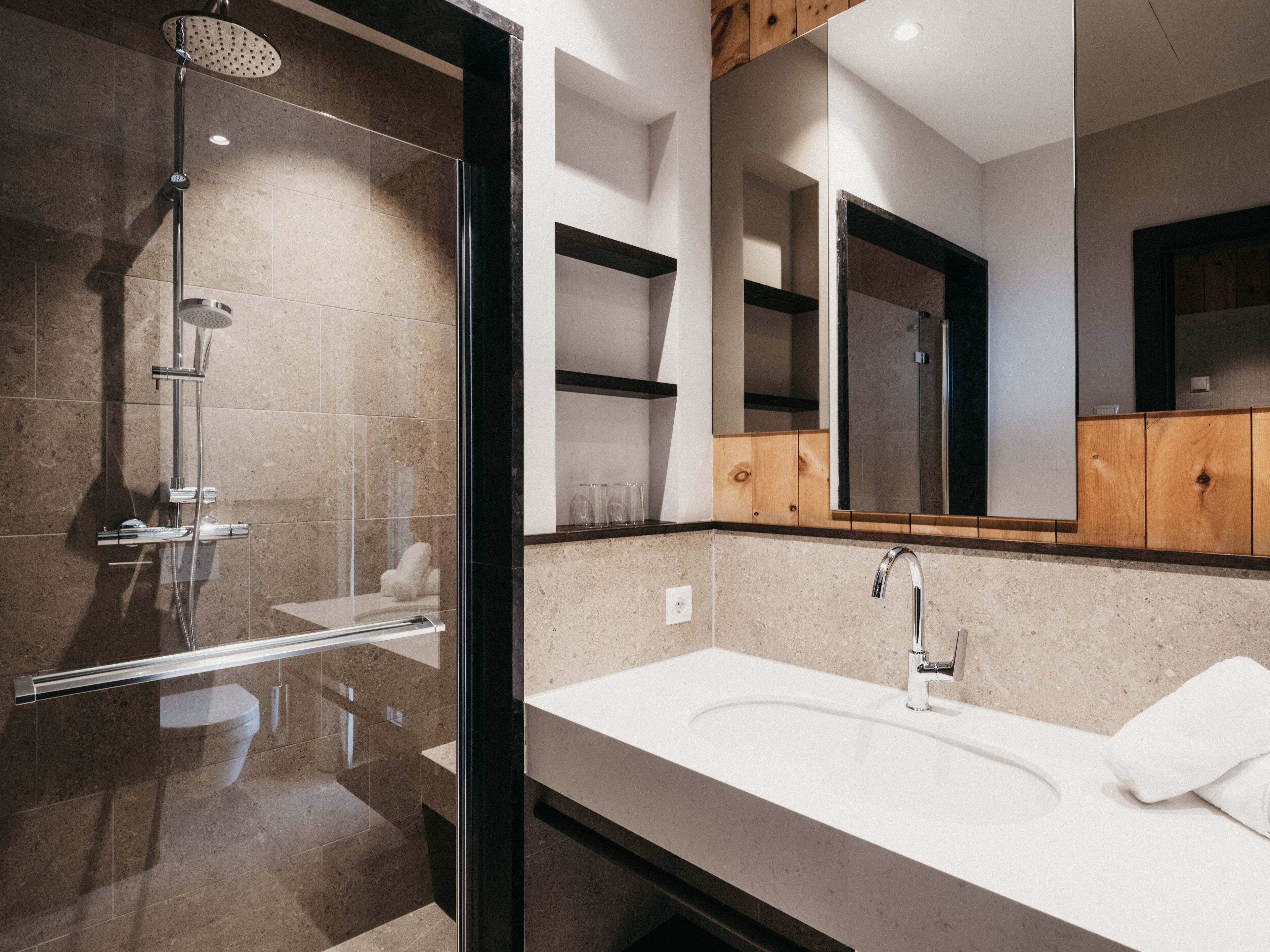 A modern bathroom with a glass-enclosed shower, a white sink, and a large mirror.