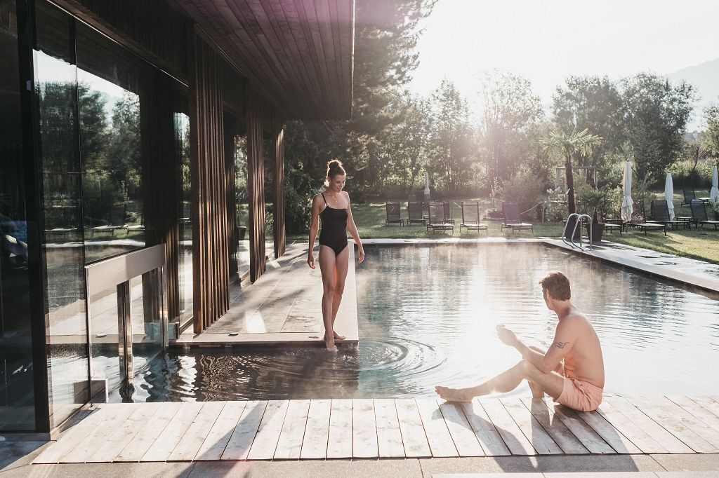 A pool area with a glass enclosure, a wooden deck, and lounge chairs.