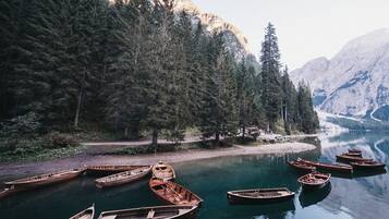 Een serene meer omringd door dicht bos en bergen. Meerdere houten boten liggen aan de oever afgemeerd.