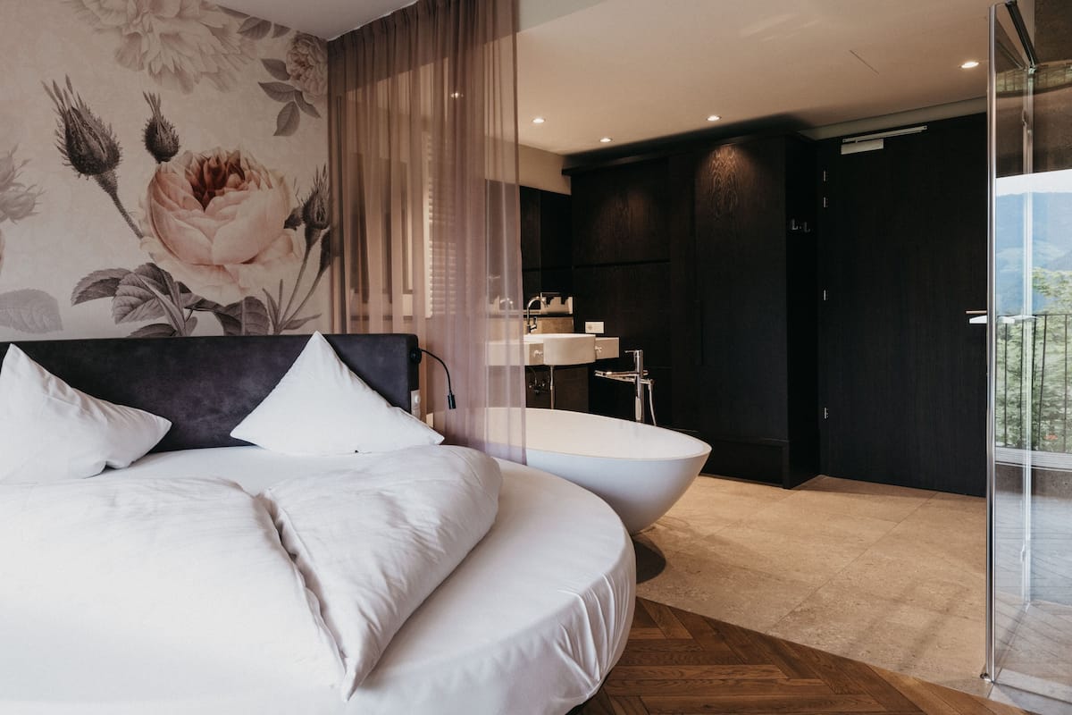 Ein Schlafzimmer mit einem großen Bett, ein Badezimmer mit einer Badewanne und Blick ins Freie.