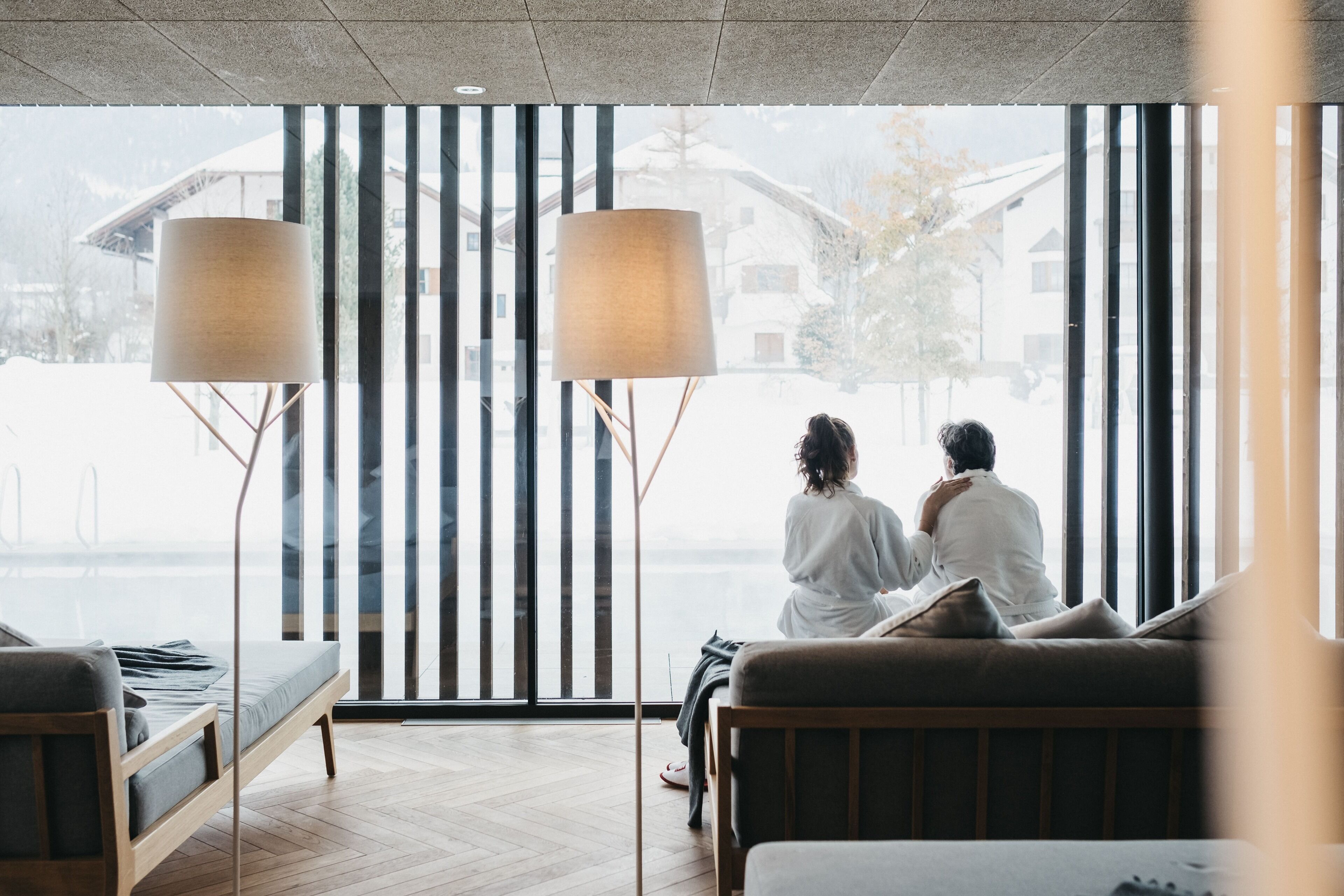A room with a large window, a sofa, and two floor lamps.