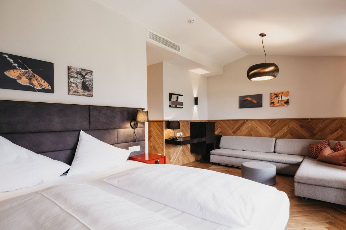 Ein modernes Hotelzimmer mit einem großen Bett, einem grauen Sofa, einem kleinen Tisch und einer Wand mit Holzverkleidung.