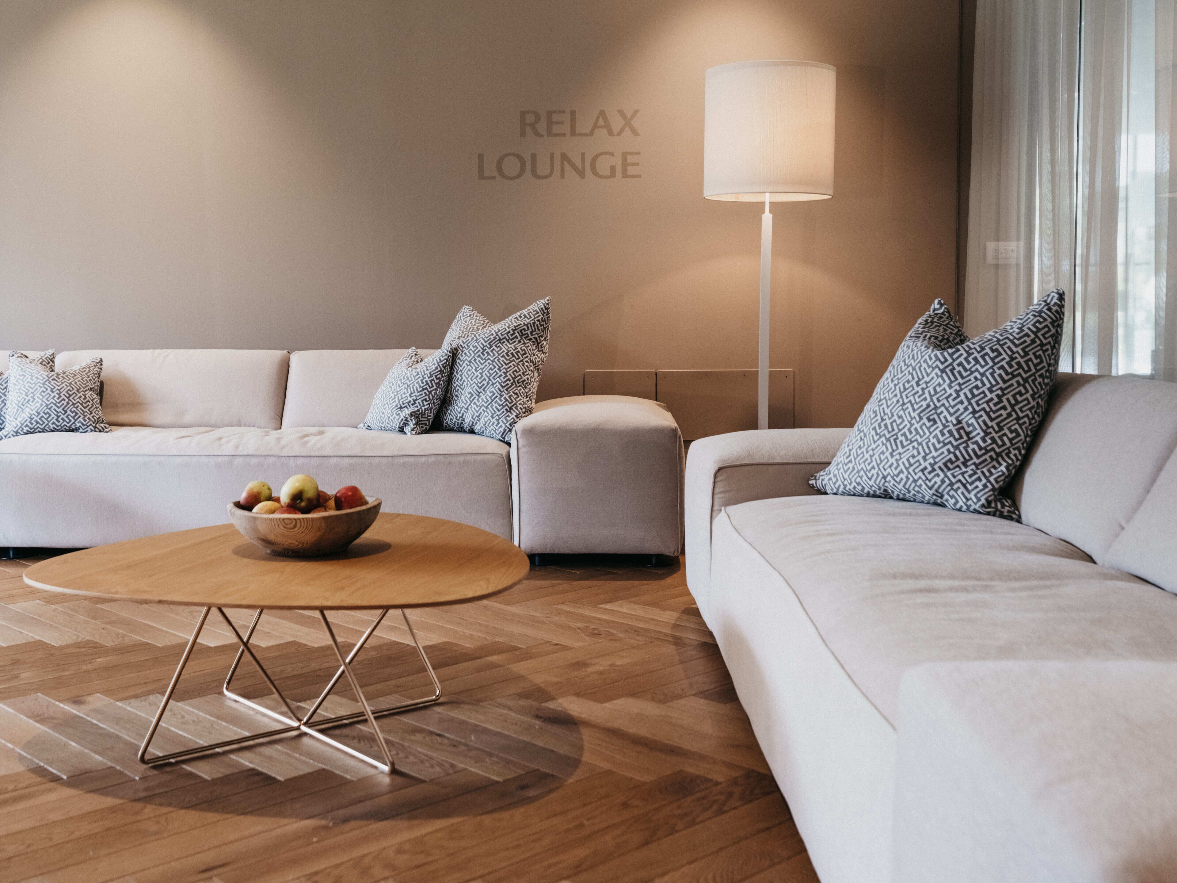A modern living room with a sofa set, a round coffee table with a fruit bowl, and a floor lamp.