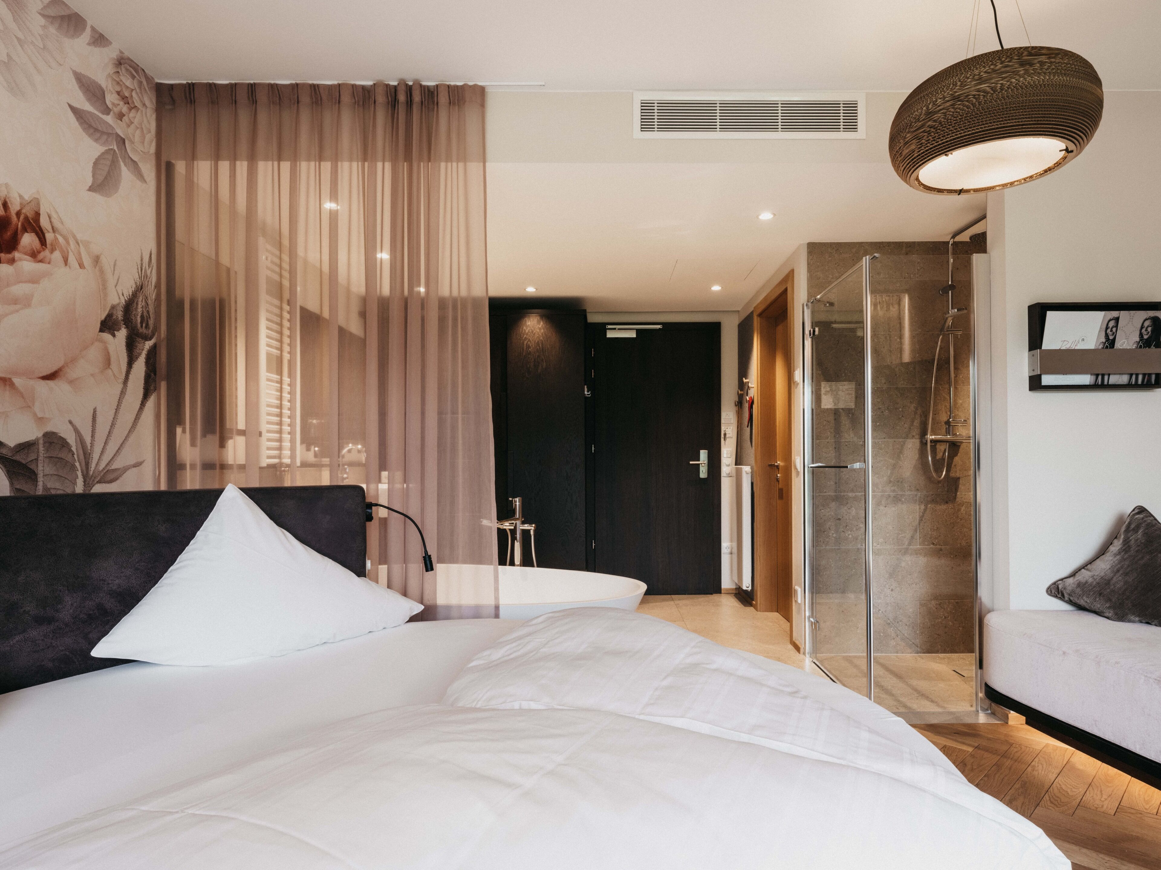 A modern hotel room with a large bed, a shower area, and a view of the hallway.