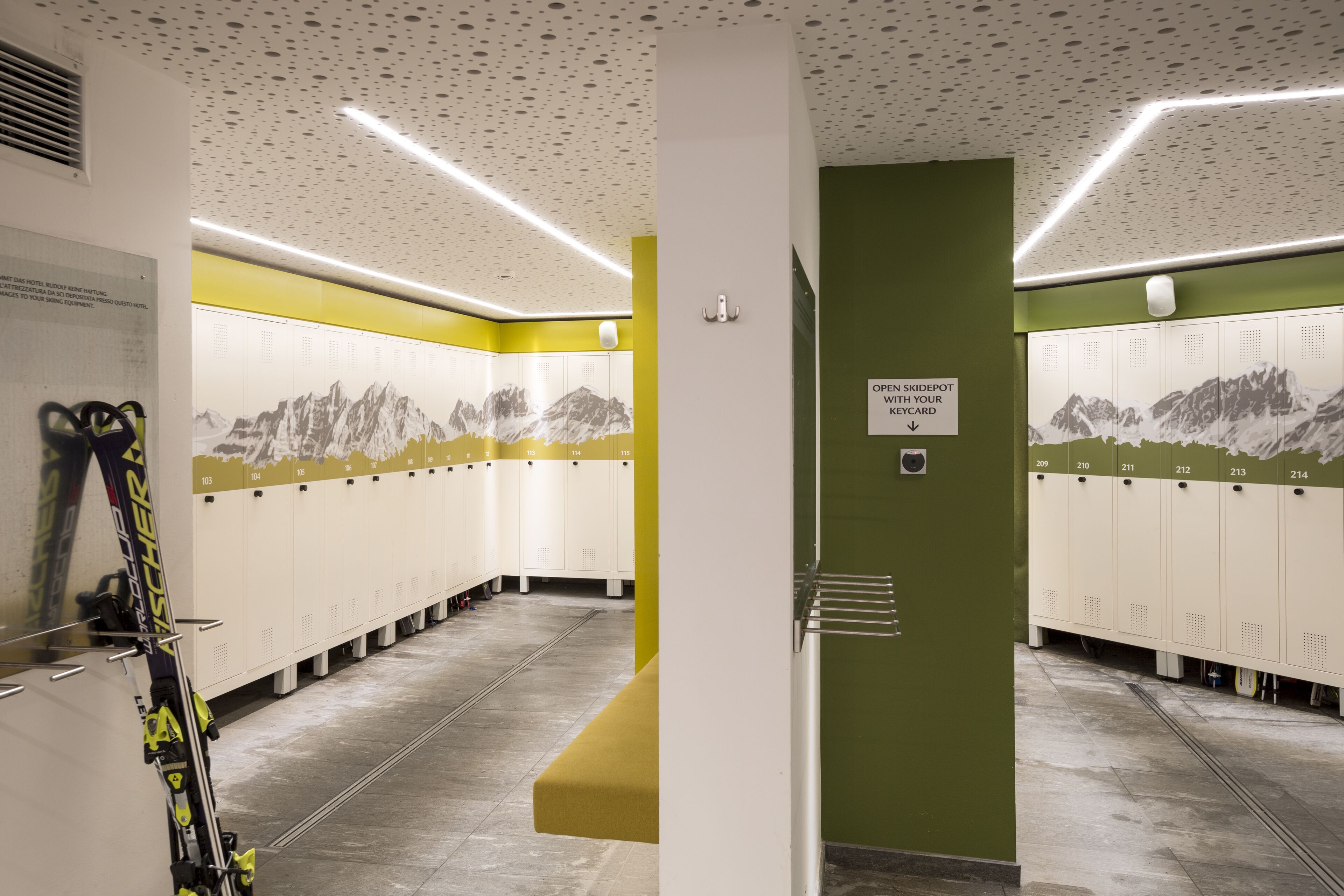 A ski resort locker room with lockers numbered 100-214, a ski rack, and a sign indicating the open ski depot with a keycard.