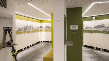 A ski resort locker room with lockers numbered 100-214, a ski rack, and a sign indicating the open ski depot with a keycard.