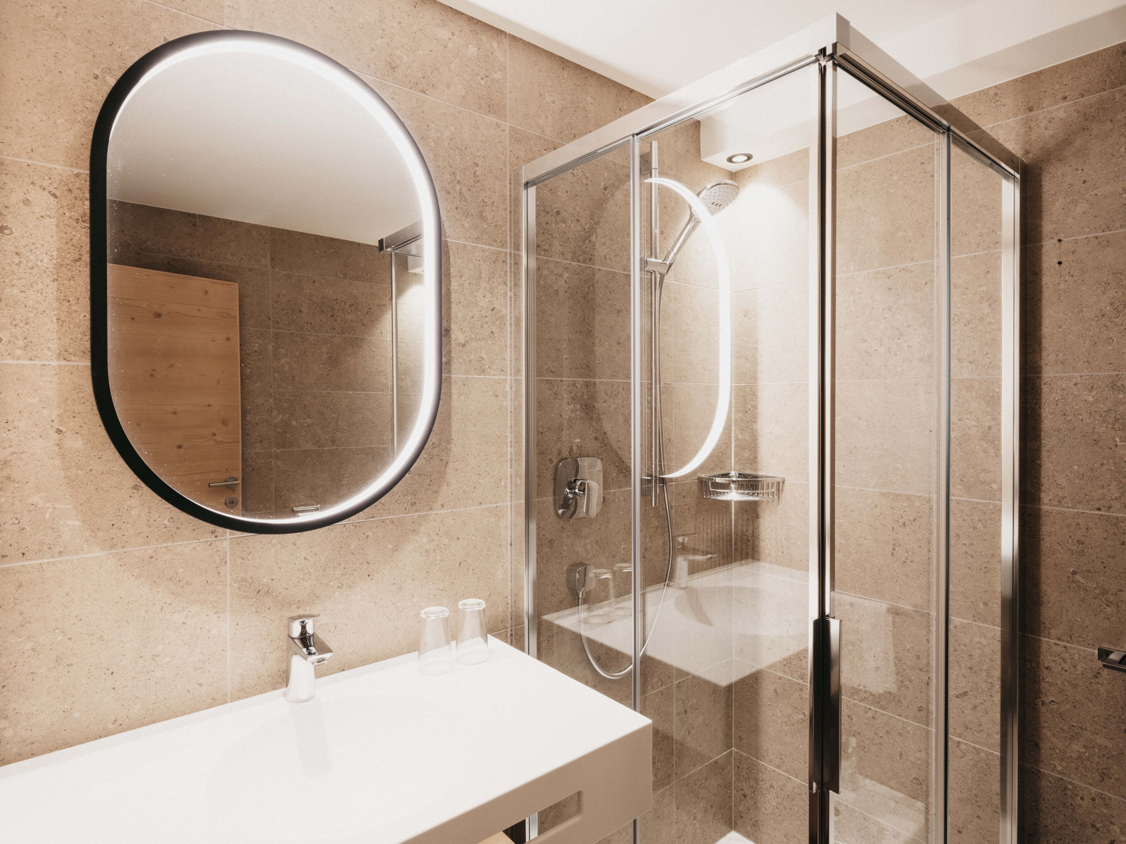Un baño moderno con cabina de ducha de vidrio, un espejo redondo y un lavabo blanco.