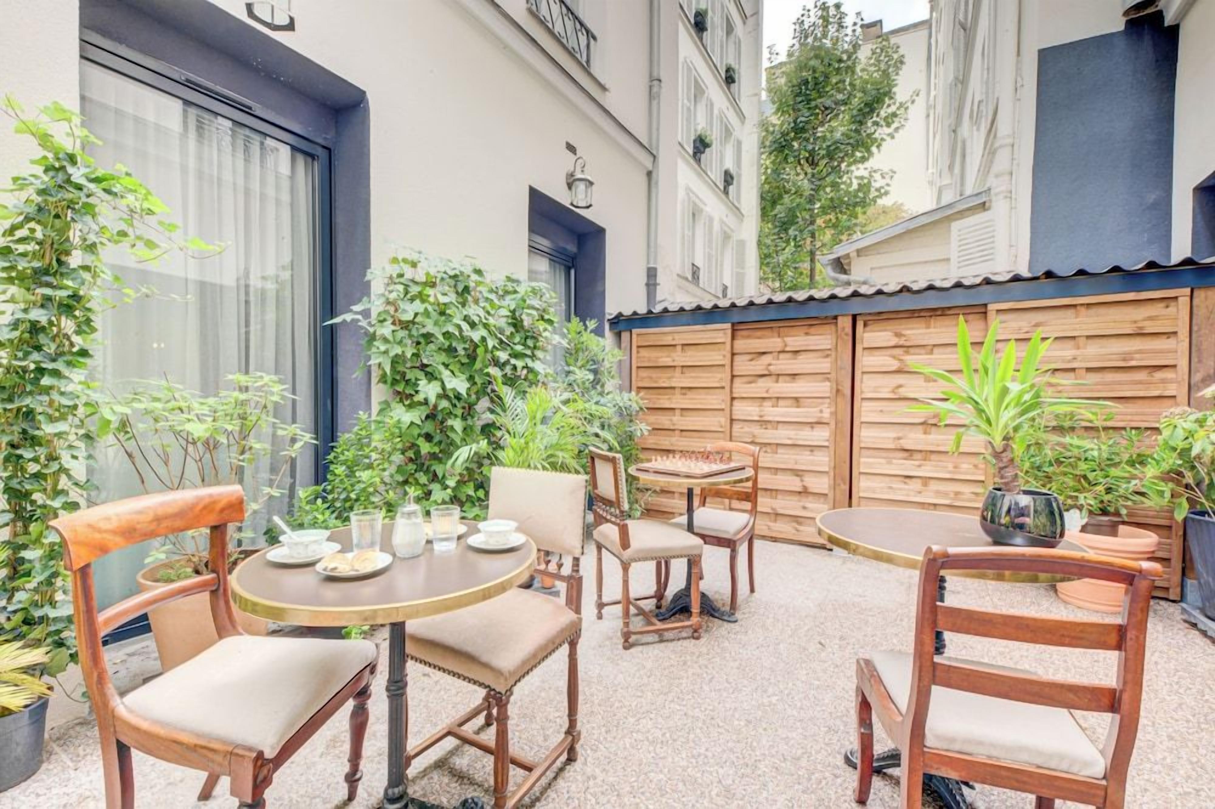 An outdoor seating area with wooden chairs and a round table, surrounded by potted plants and a wooden fence.