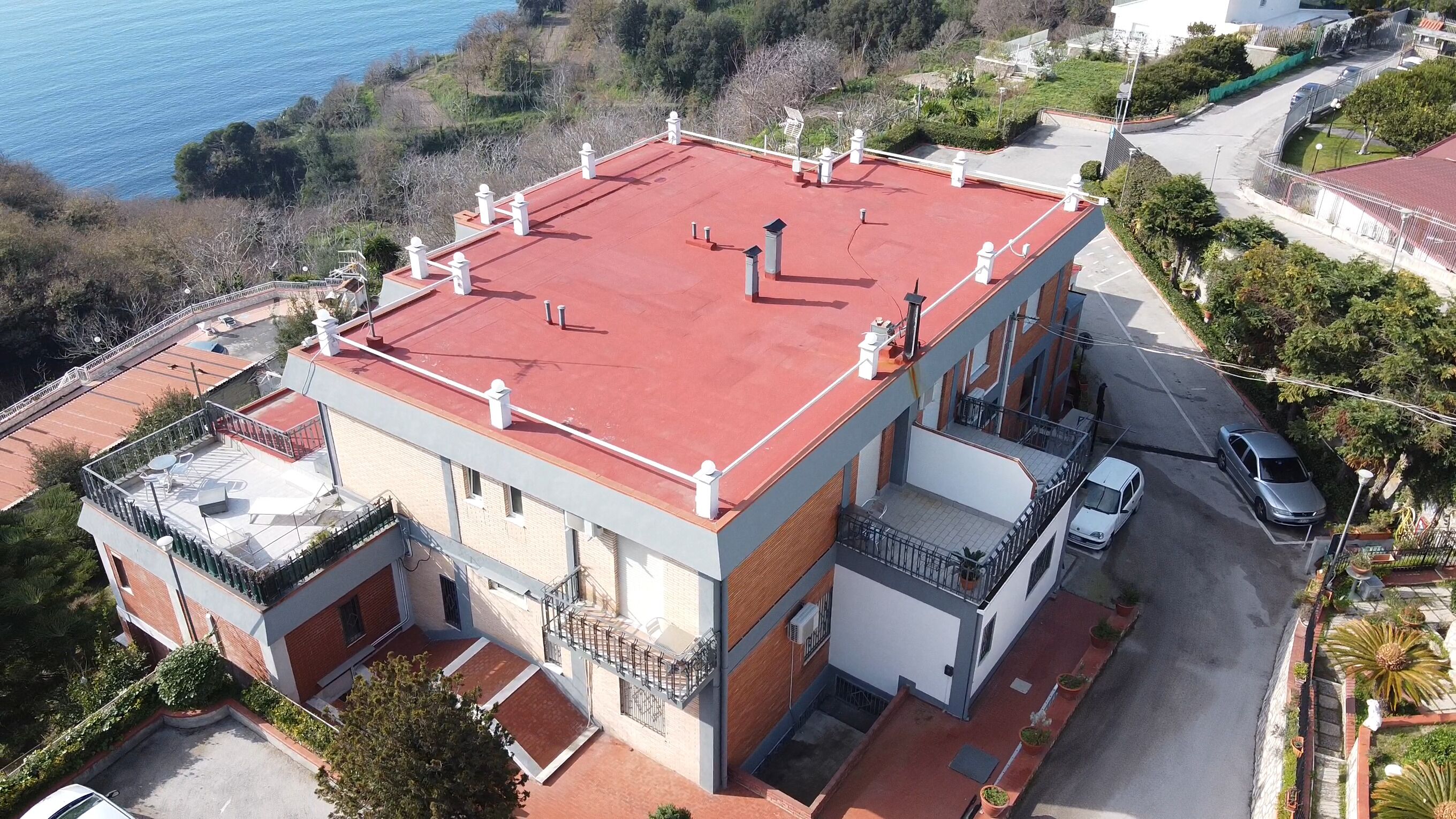 A two-story building with a red roof, a balcony, and a parking area.