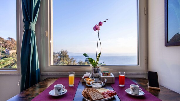 A breakfast table with a view of the sea, a vase with flowers, and a smartphone on a stand. - Mini Hotel (Pozzuoli)